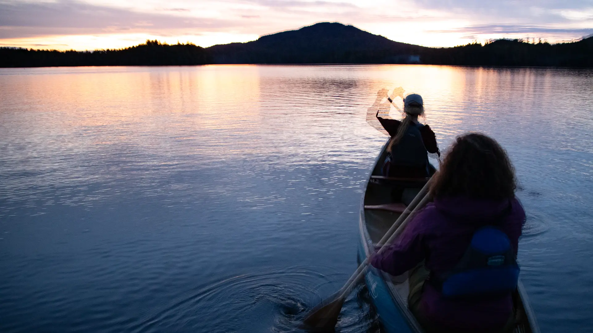 Two people canoeing towards the sunset on Lower Saranac Lake