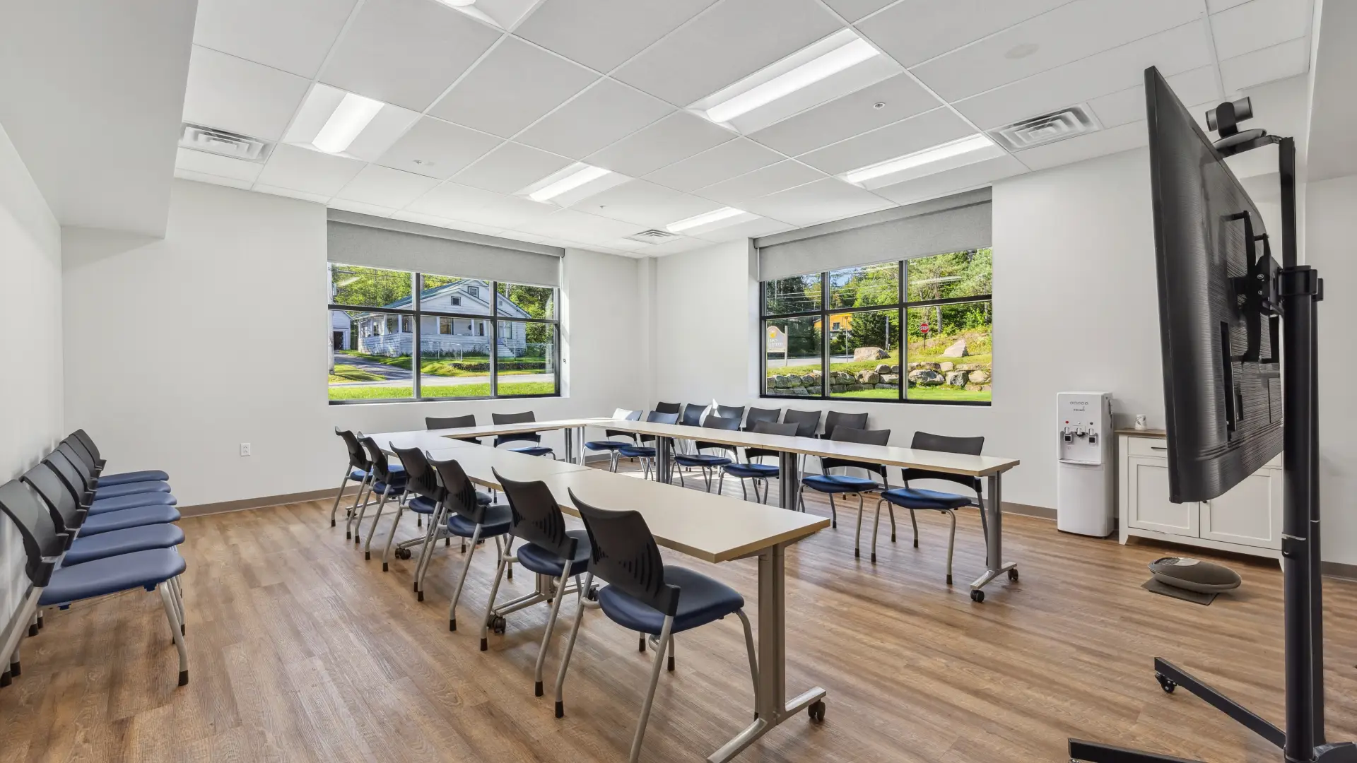 The meeting space arranged in a U shape with chairs and a large screen on a mount, viewed from the doorway.