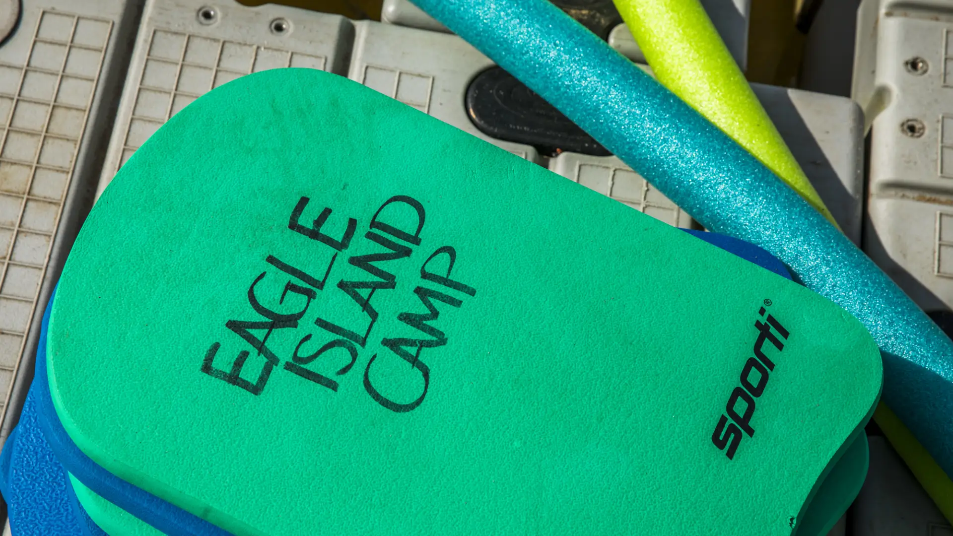 Colorful pool noodles and kick boards with Eagle Island Camp emblazoned.