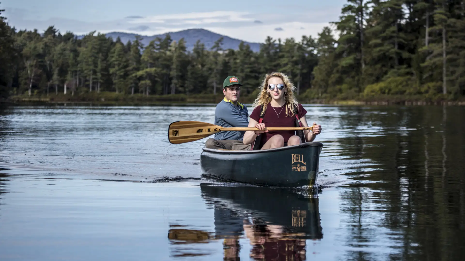 Two people canoeing on a lake surrounded by trees