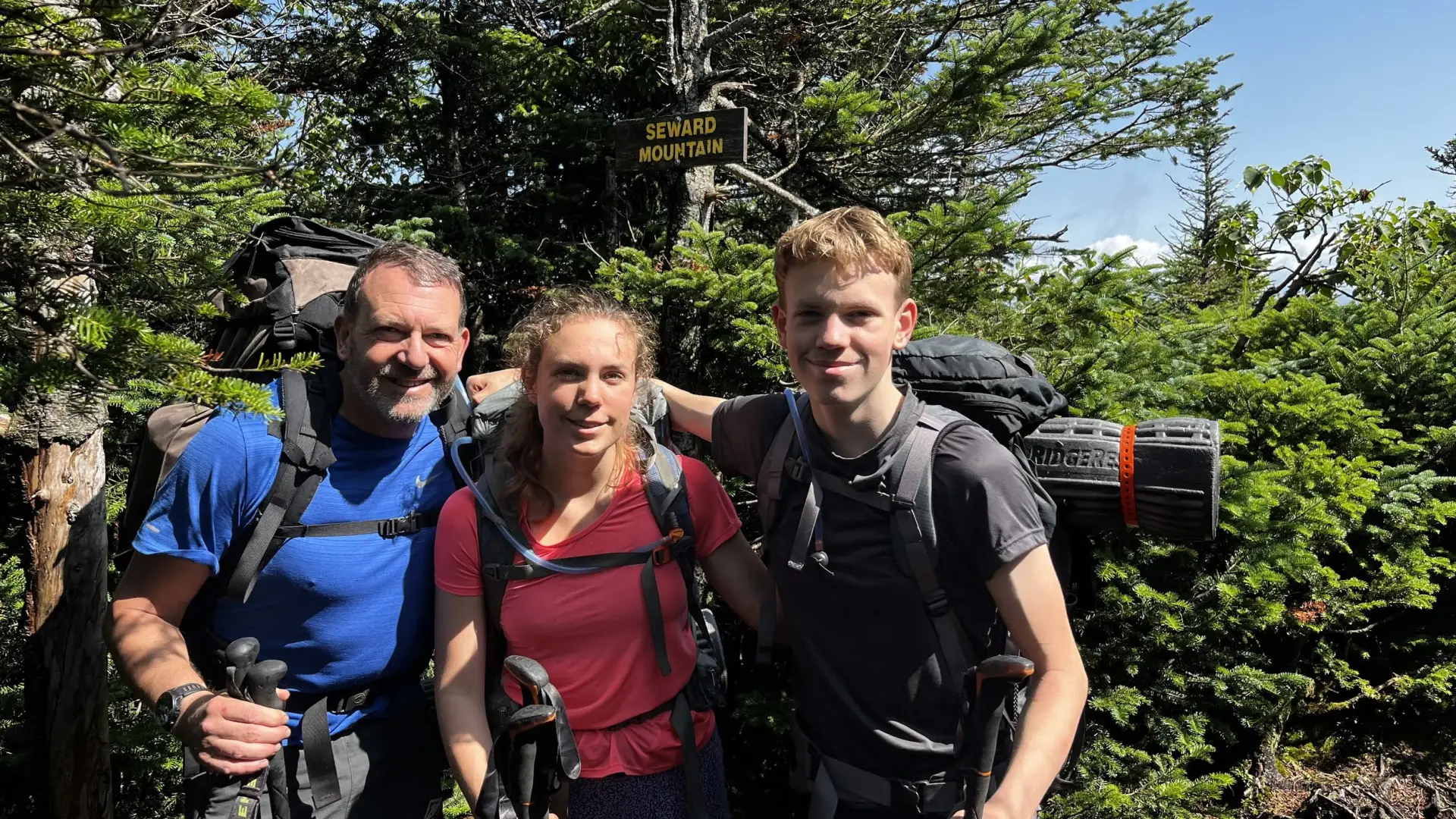 A group smiles with their camping gear at the summit of Seward Mountain