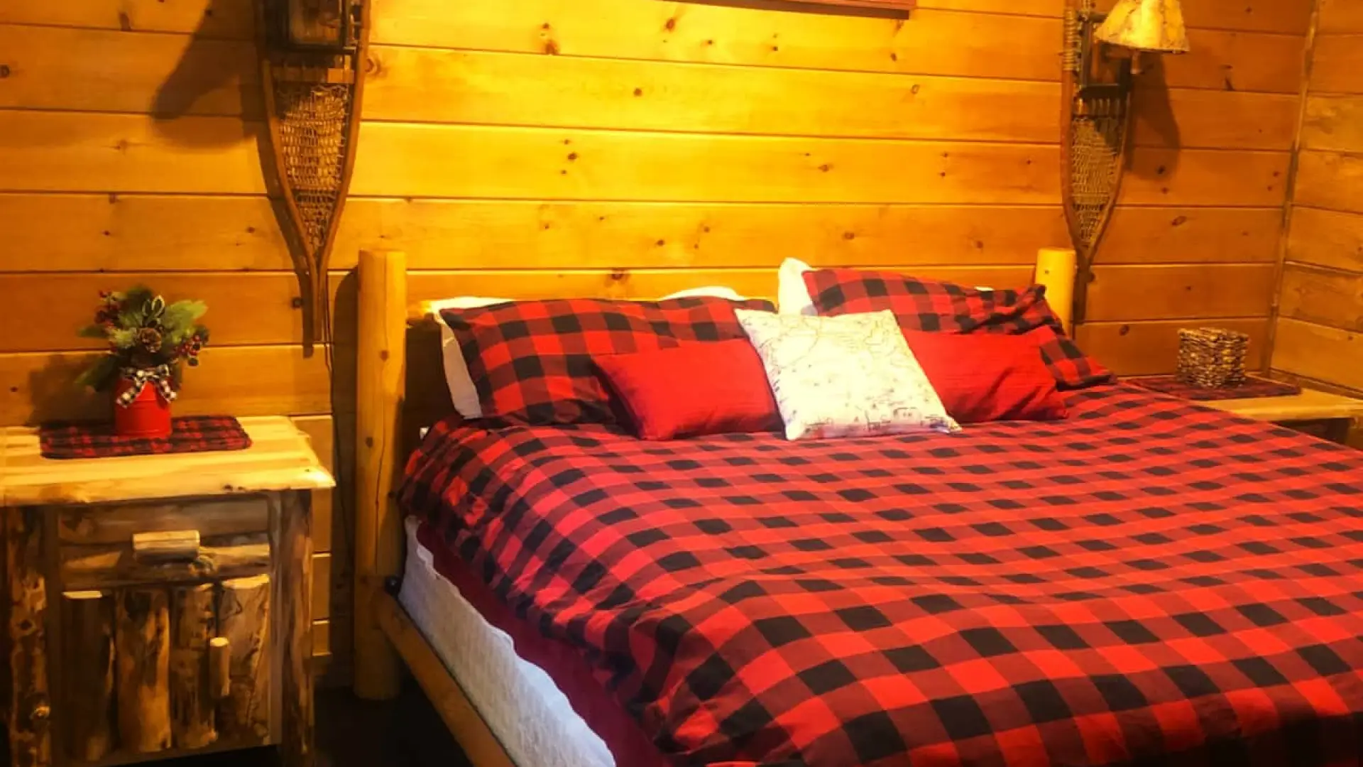 A bedroom with knotty pine paneling, snowshoe sconces and buffalo plaid style bedding.
