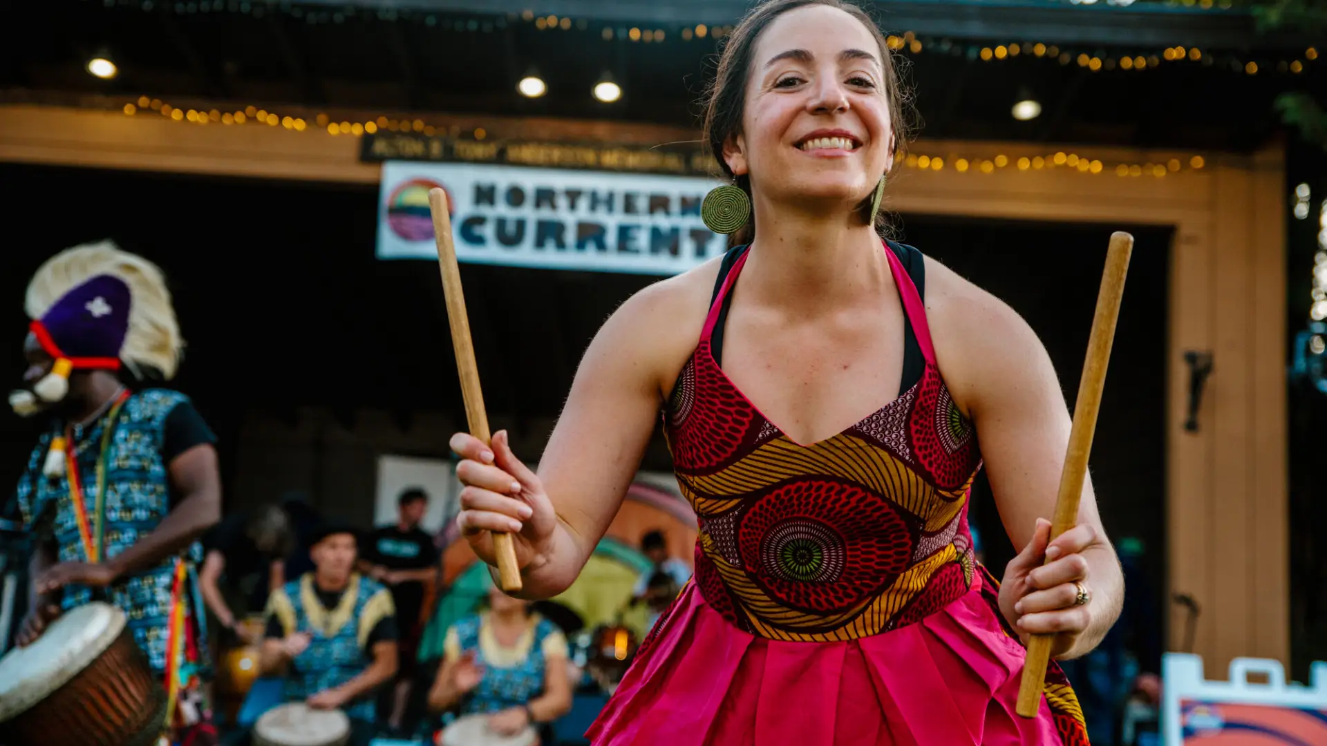 A friendly drummer in a colorful dress smiles into the crowd