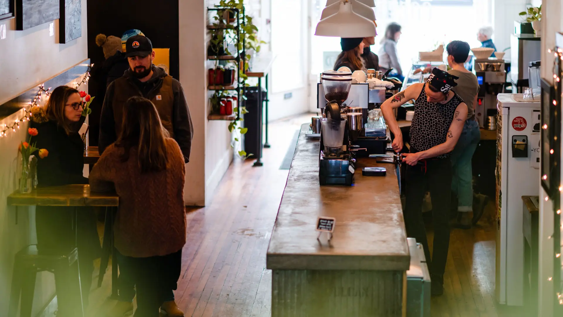 Barista prepares to pull a freshly ground espresso shot on a live edge bar while patrons mingle.
