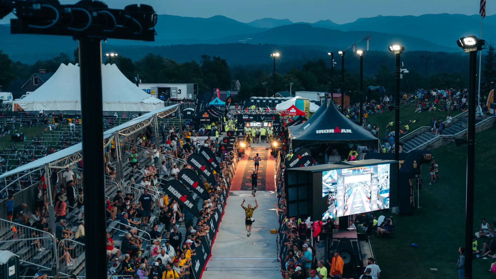 Ironman athletes approach finish after dark with faint mountains in distance