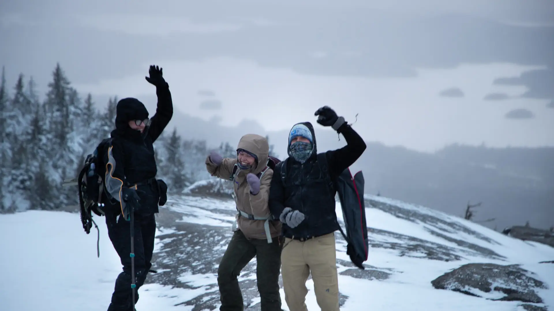 Three hikers cheering at the summit of Ampersand Mountain in the winter