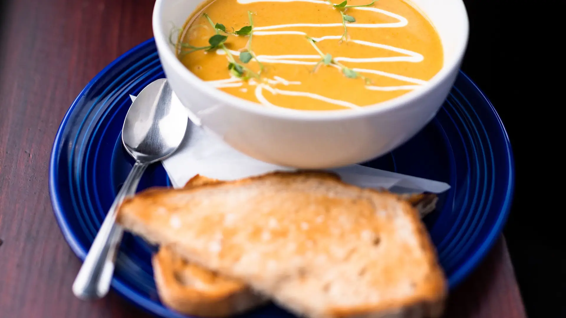 Creamy squash soup in a white bowl with toasted bread on a blue plate with spoon.