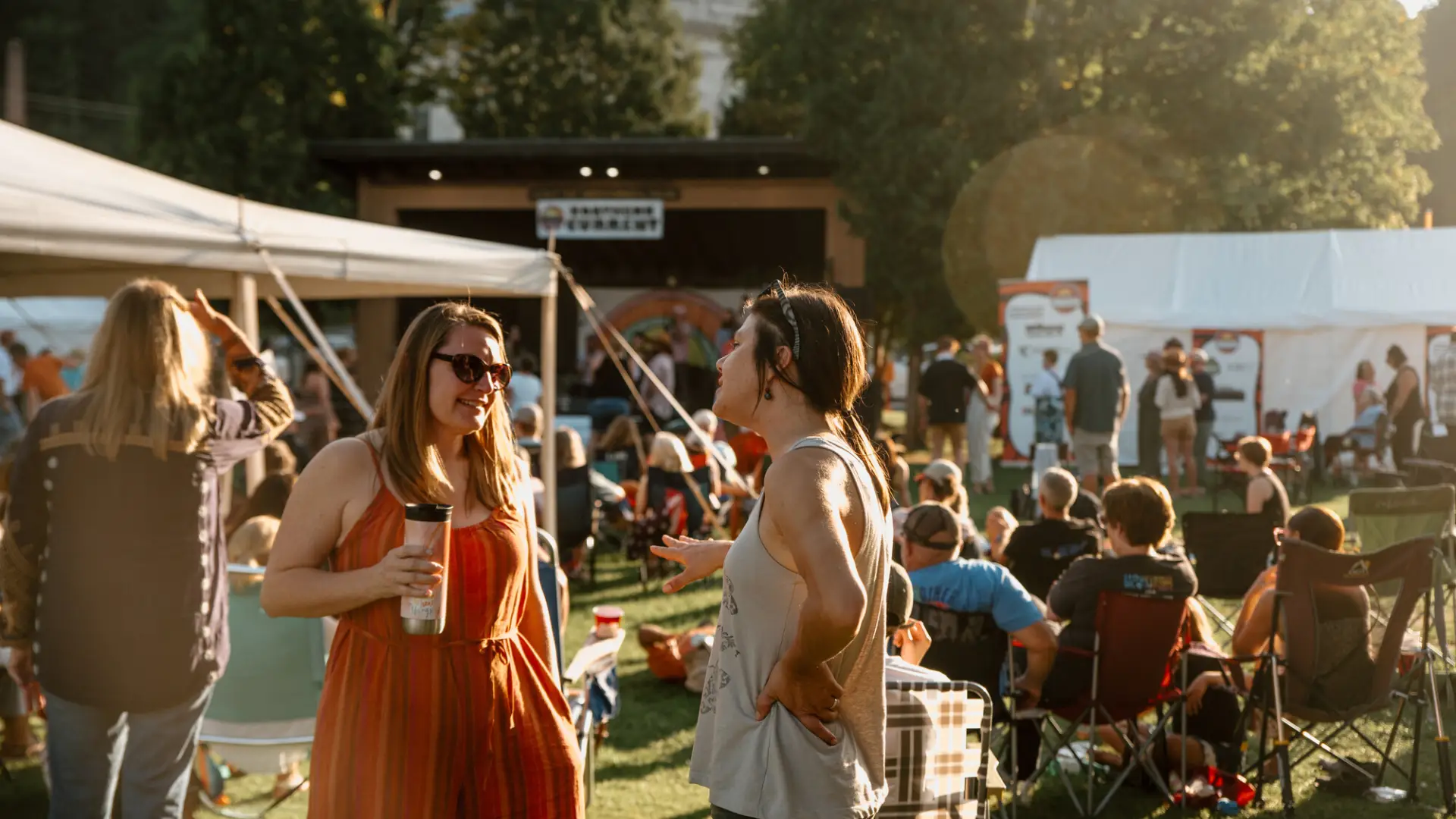 Women socialize surrounded by people in lawn chairs and at vendor booths