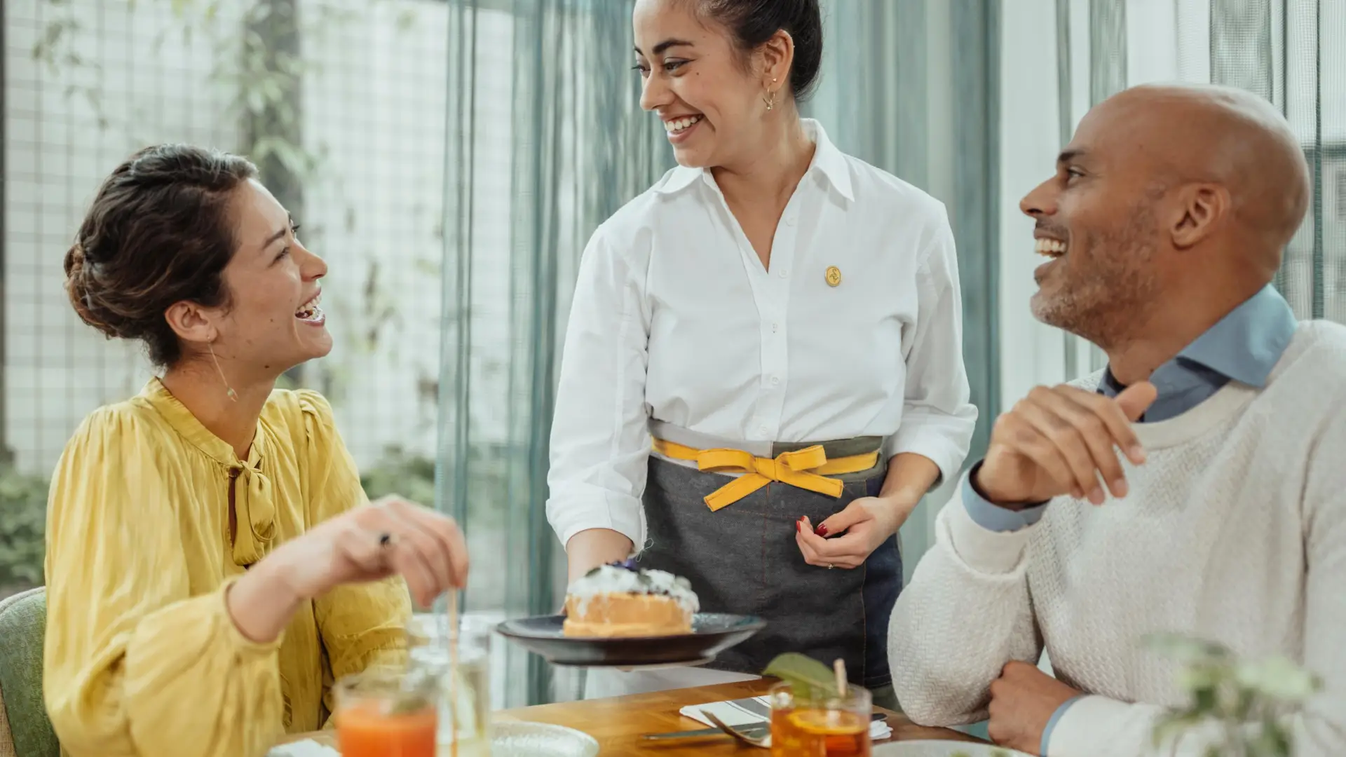 A server laughs with the couple at the table surrounded with delicious foods
