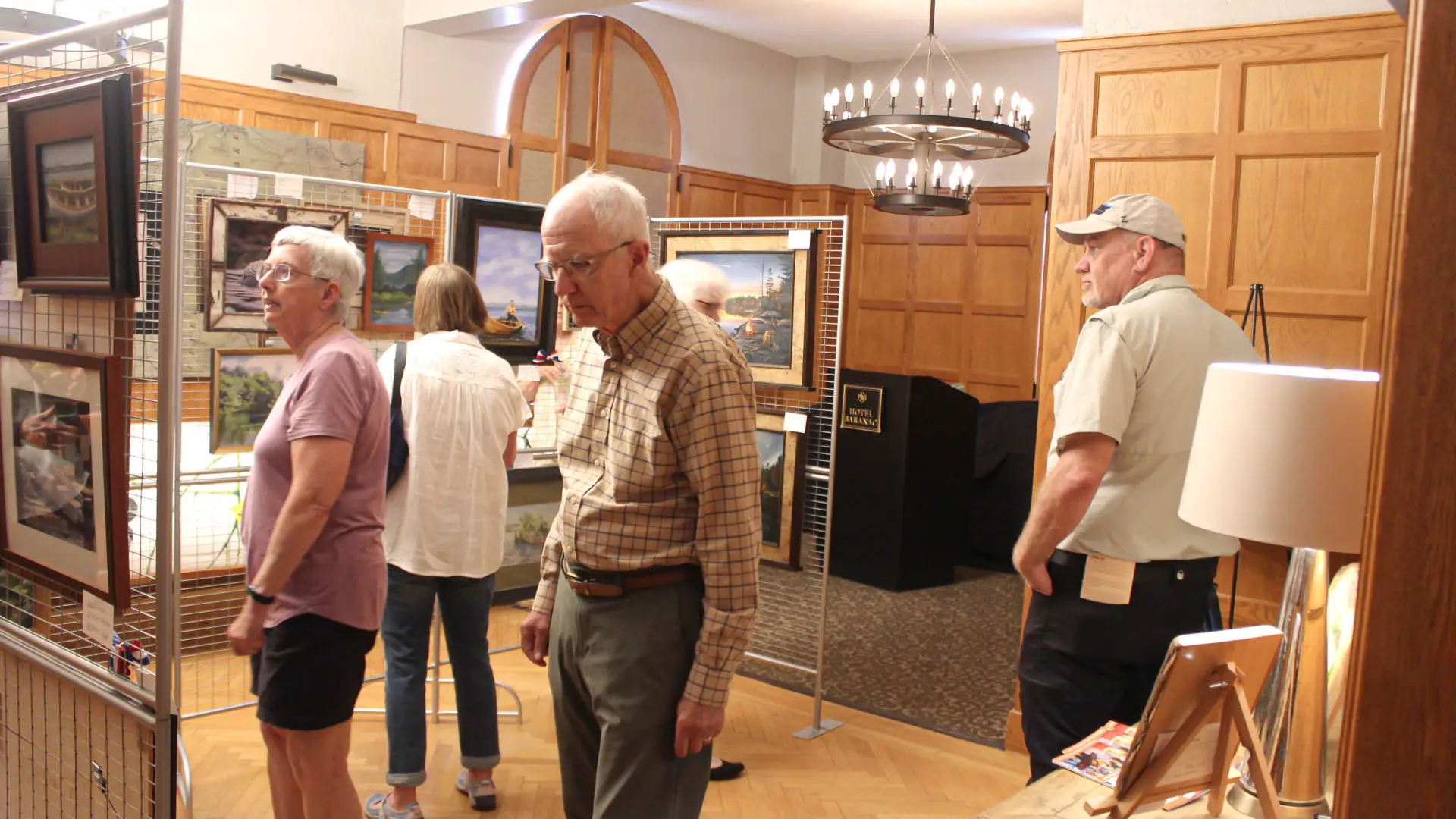 People observe the art inside a large room with wood paneled walls at the guide boat art show