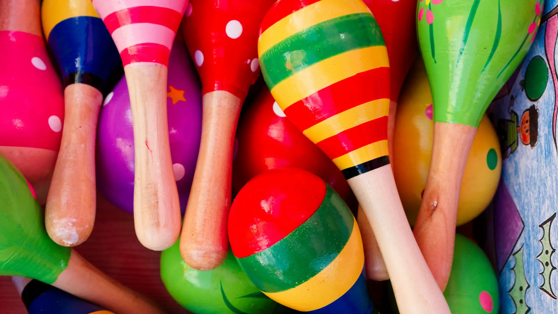 A vibrant, close-up overhead view of a pile of brightly colored, hand-painted wooden maracas featuring various patterns.