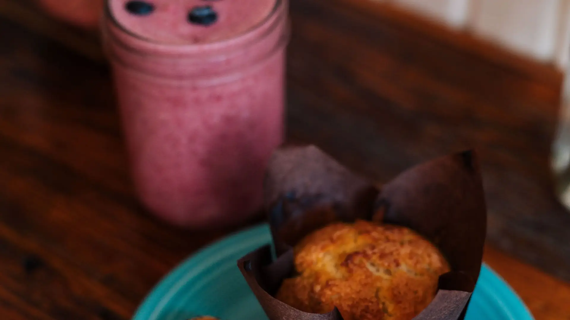 Muffin and croissant on a plate next to a berry smoothy.