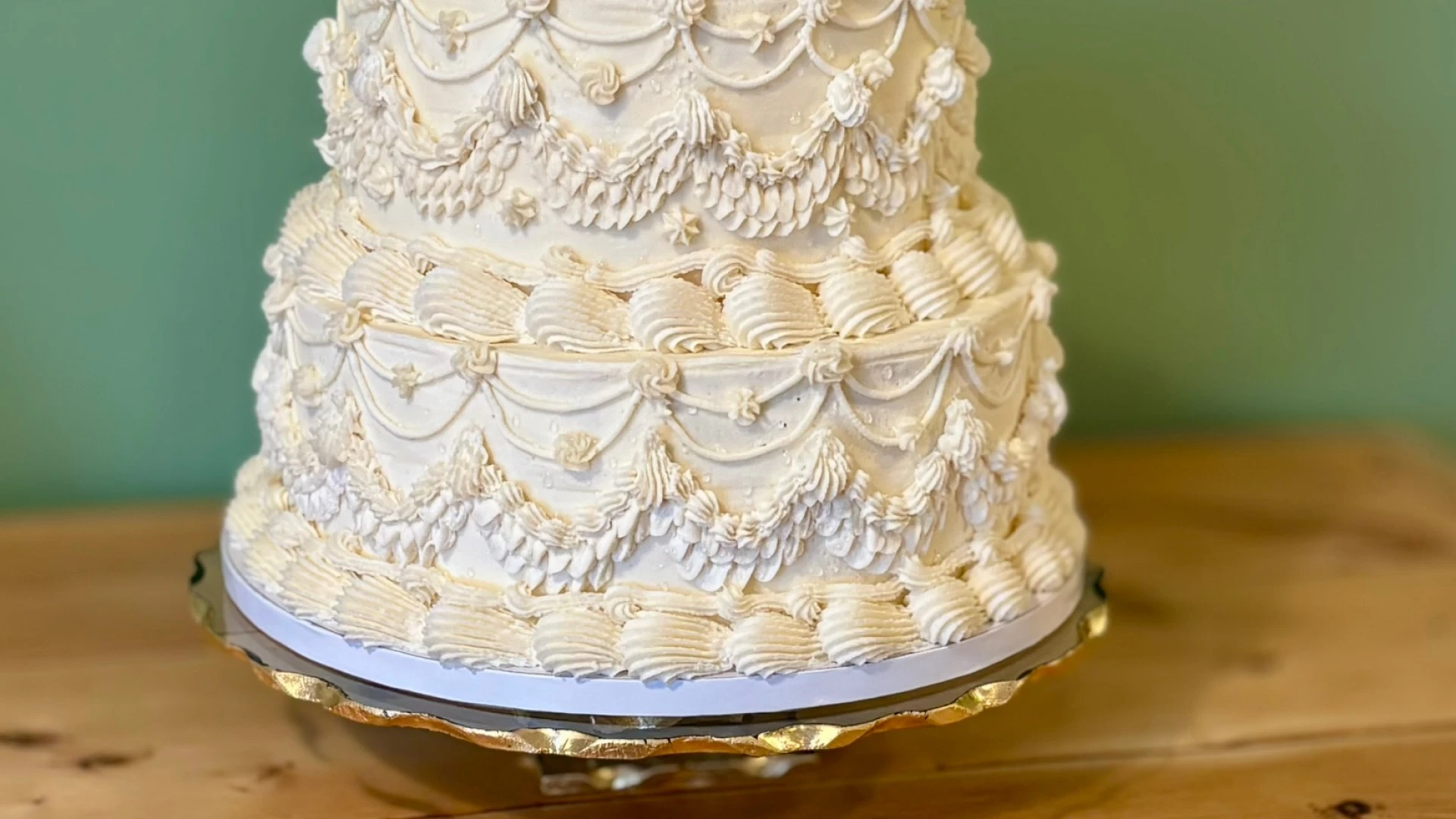 A two tier cake decorated with layers of ornate white draped piping.
