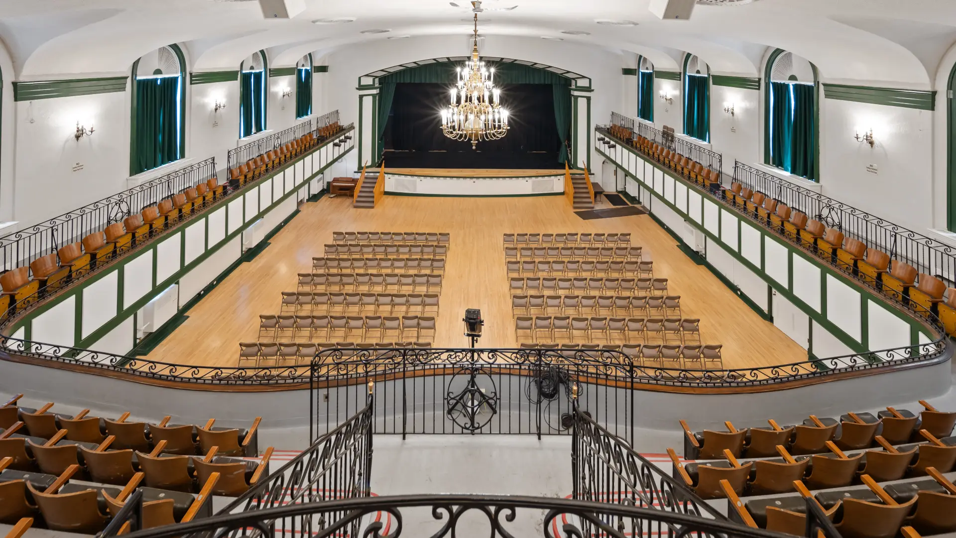 The auditorium with balconies and raised, curtained stage at the Harrietstown Town Hall, viewed from the balcony