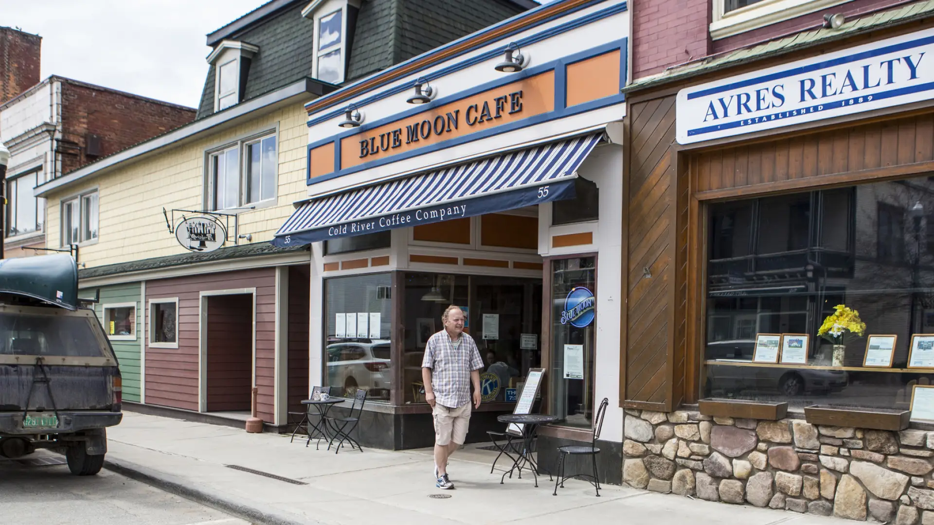 A man walks out of a cafe onto a main street. 