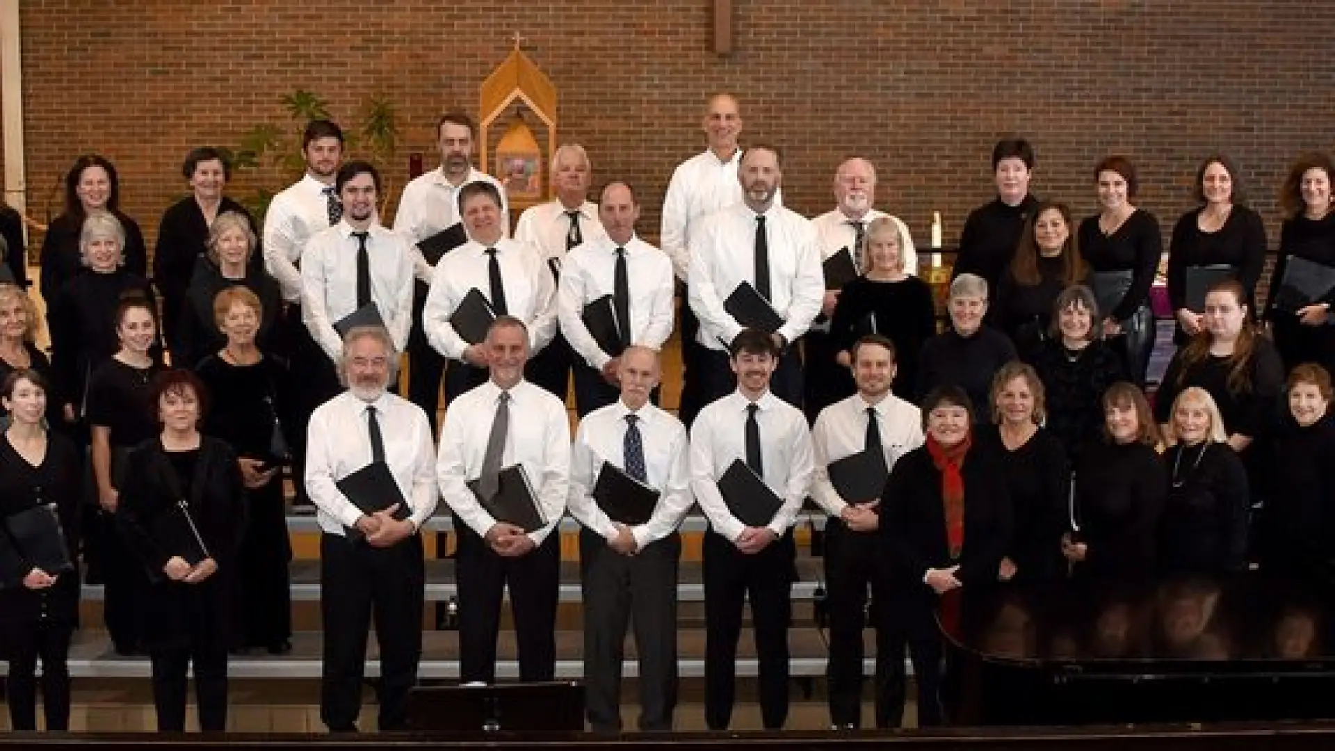 The mens choir stands on stage with white shirts, black ties and pants.