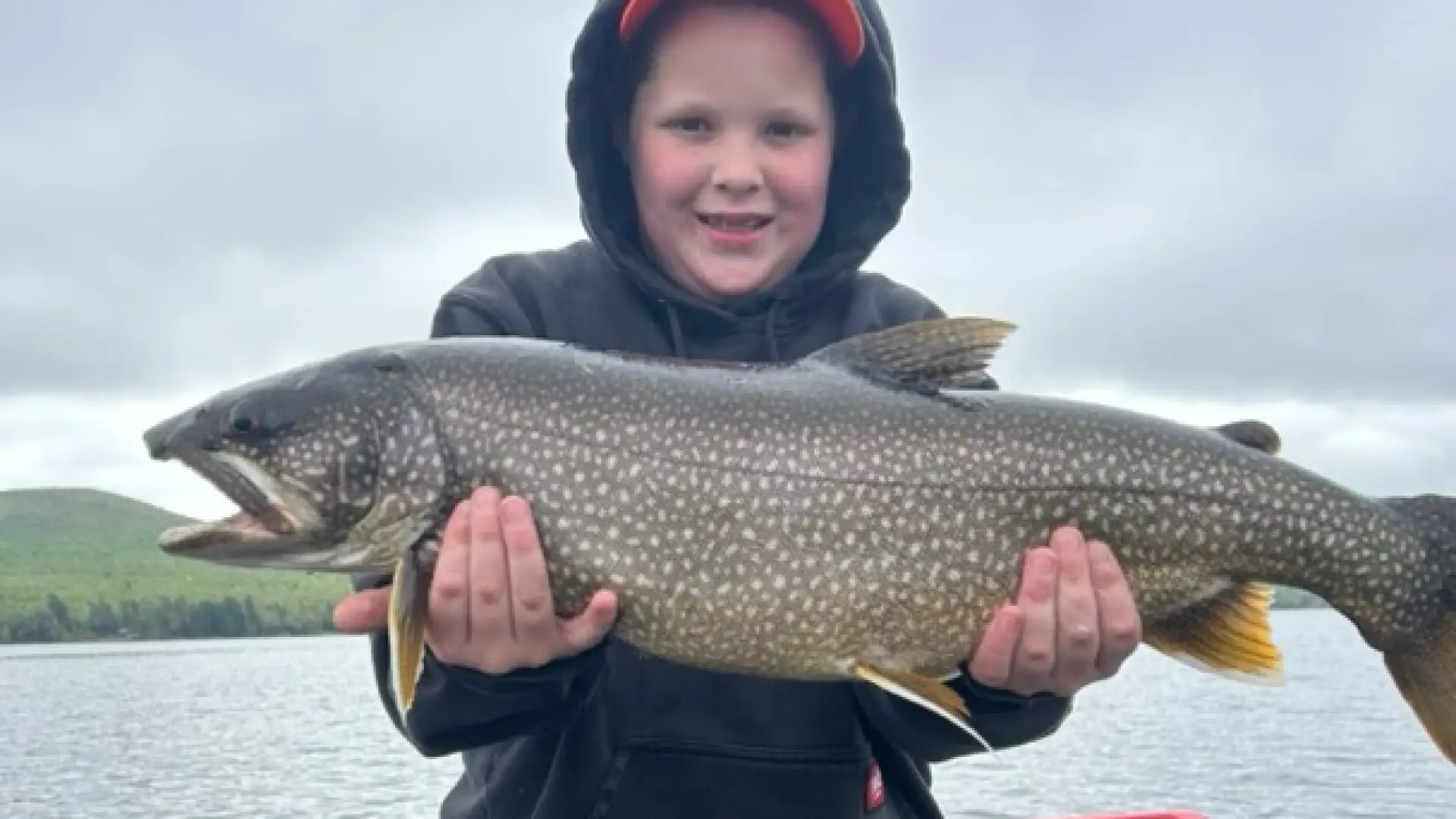 A smiling kid standing on a boat holding a large fish.