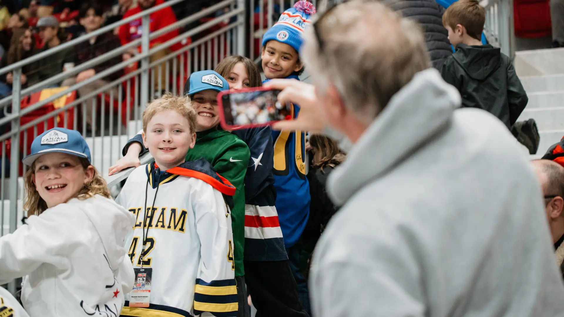 Older man takes photo of kids in hockey jerseys in crowd at hockey game in 1980 Herb Brooks Arena