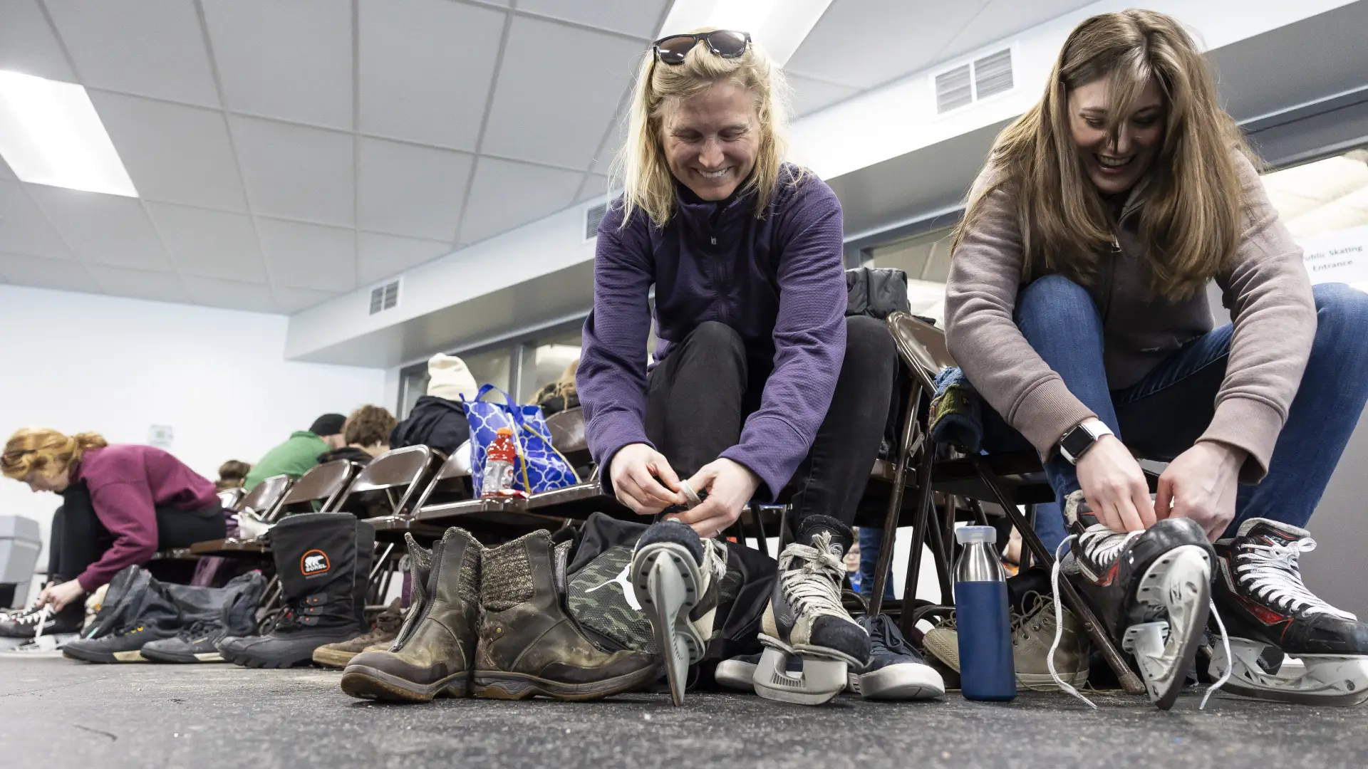 People putting on ice skates and leaving piles of shoes under chairs.