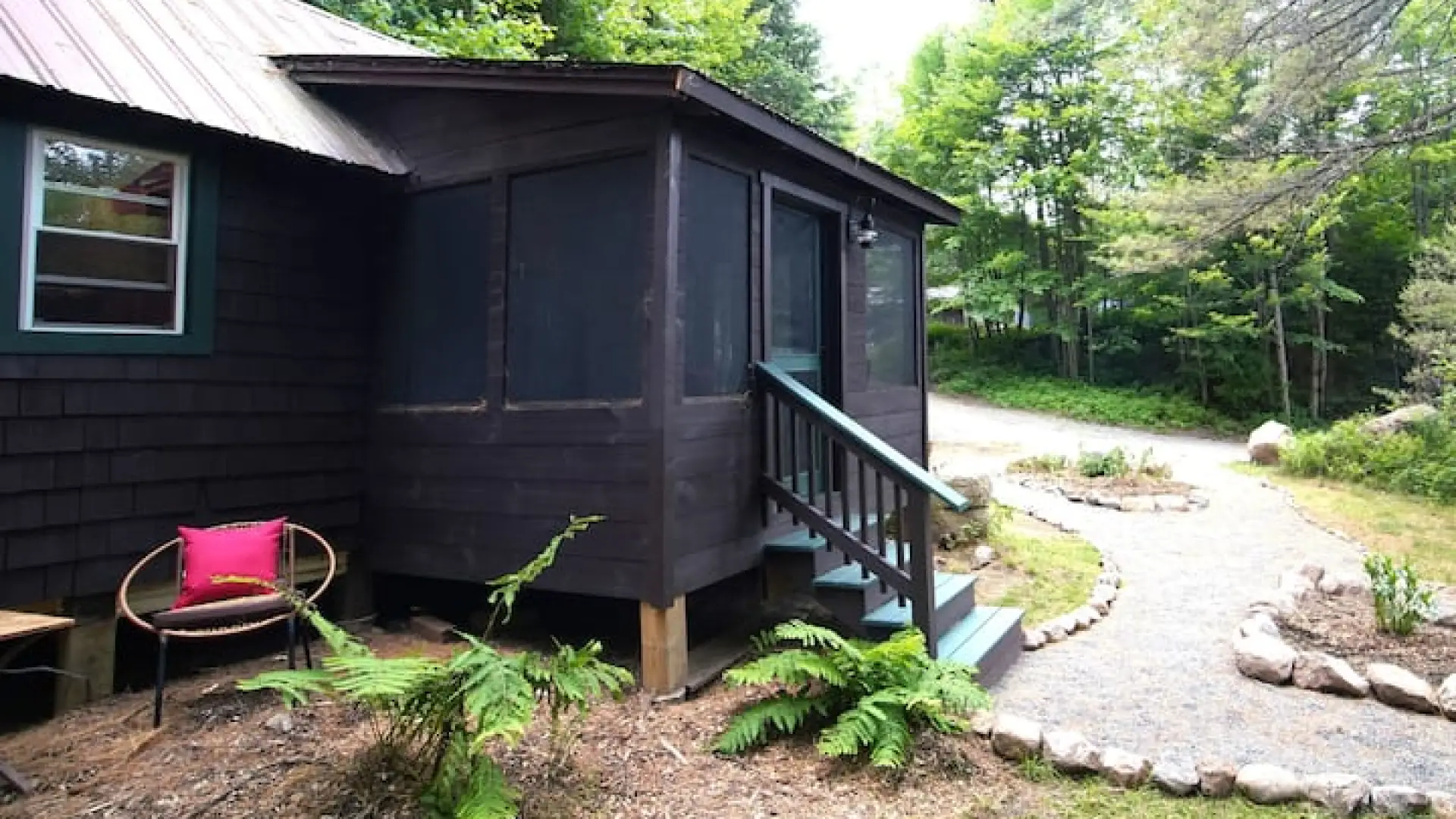 A dark brown cabin sits at the base of a driveway in the woods.