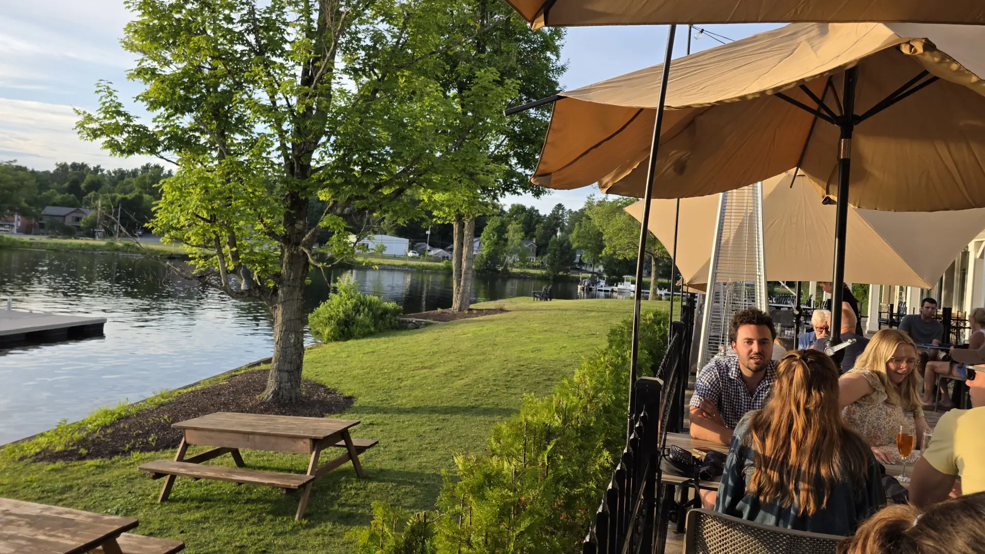 The dining patio next to a swath of grass with picnic tables and the waterfront of Lake Flower