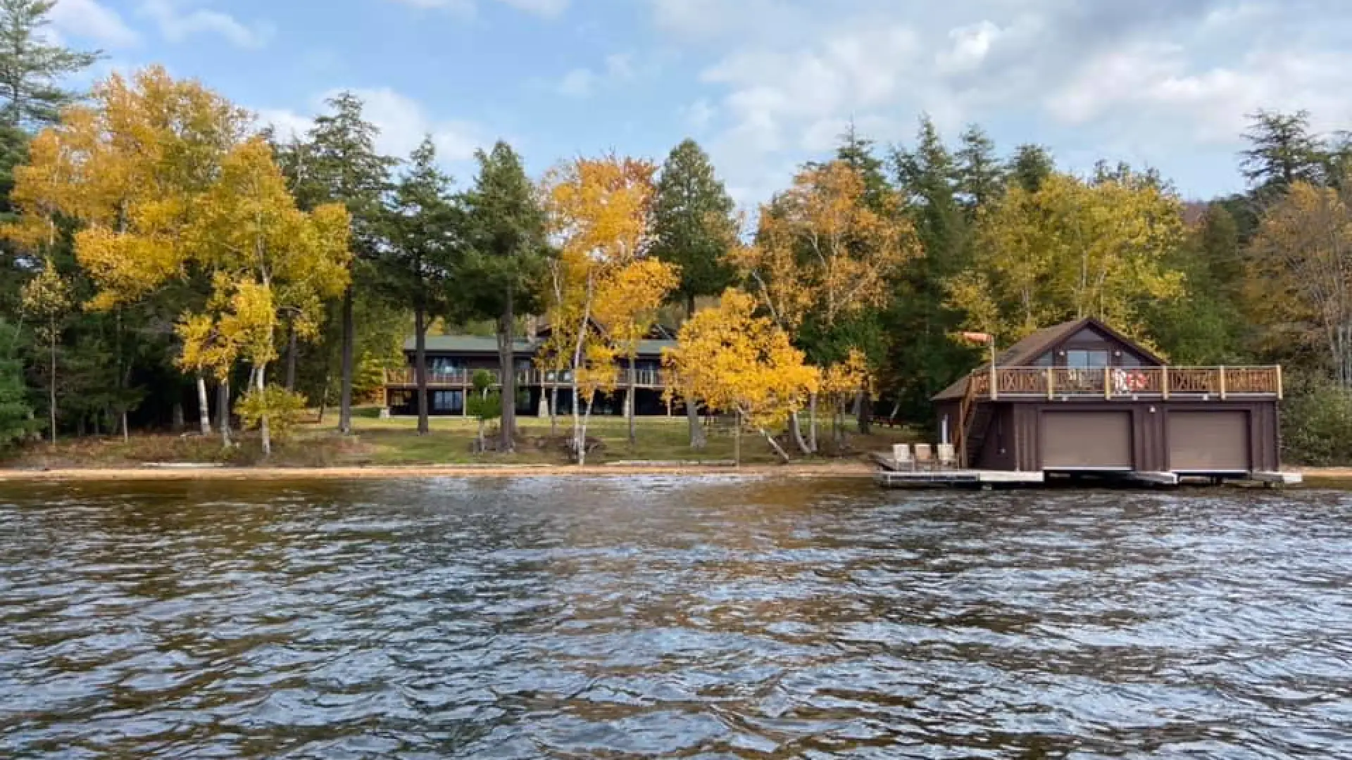 A view of the Alpenglow Lakeside Lodge with prominent boathouse from in the water in early fall when the birches turn yellow.