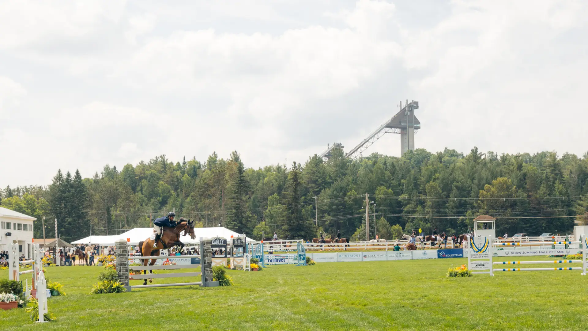 A Horse and rider jump the gates with the jumping complex ski jump over head in the background.