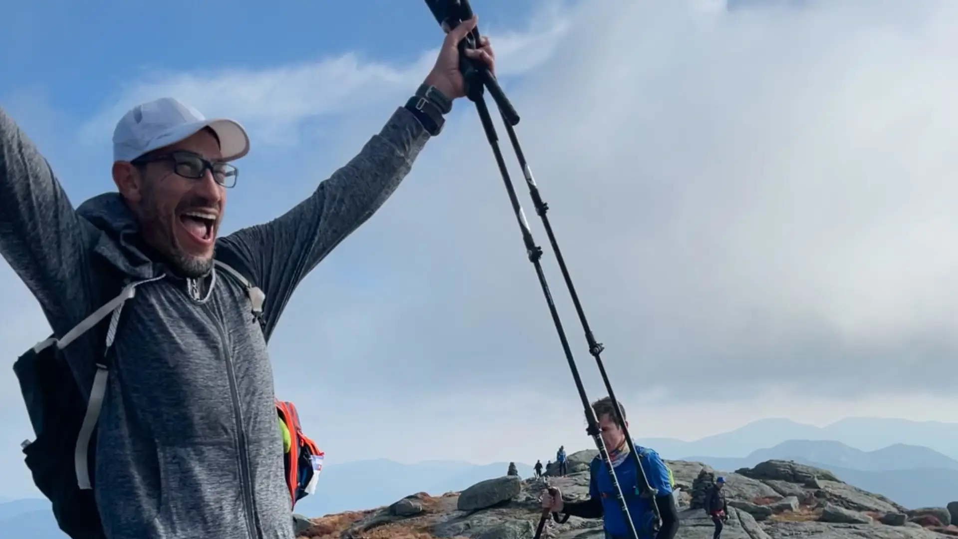 A very happy man raises his arm in sucess at the top of the summit