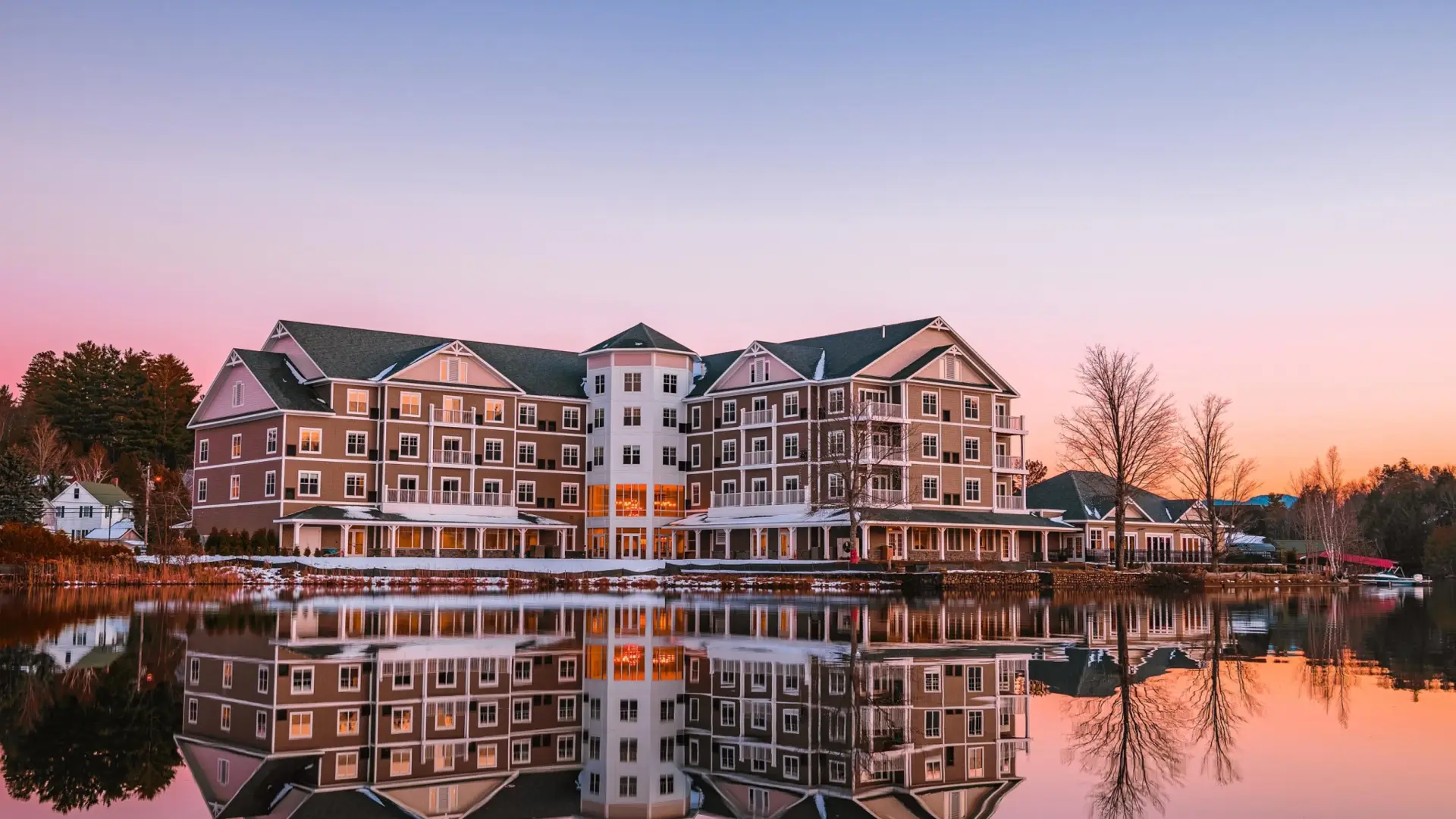 A sprawling hotel sits on the edge of a lake in early winter with the sun rising in the background. 