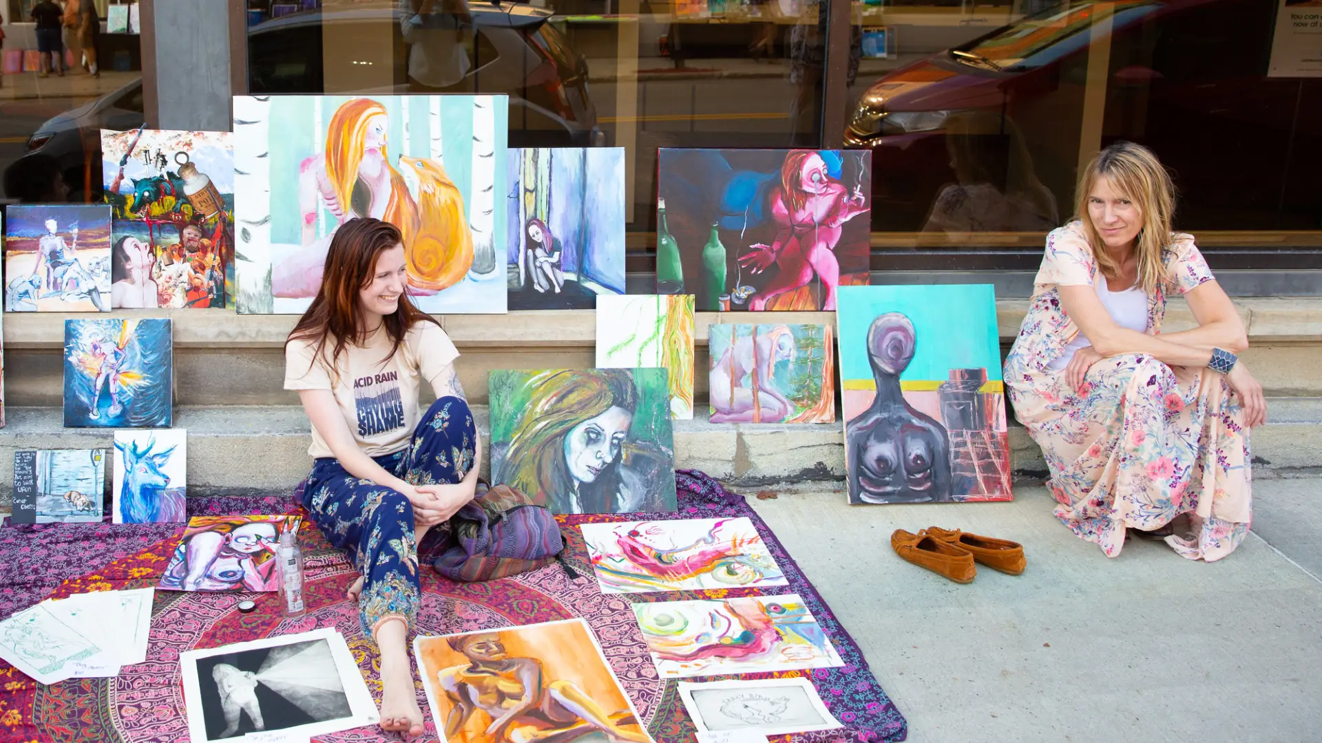 Two women showcase their art on the sidewalk.
