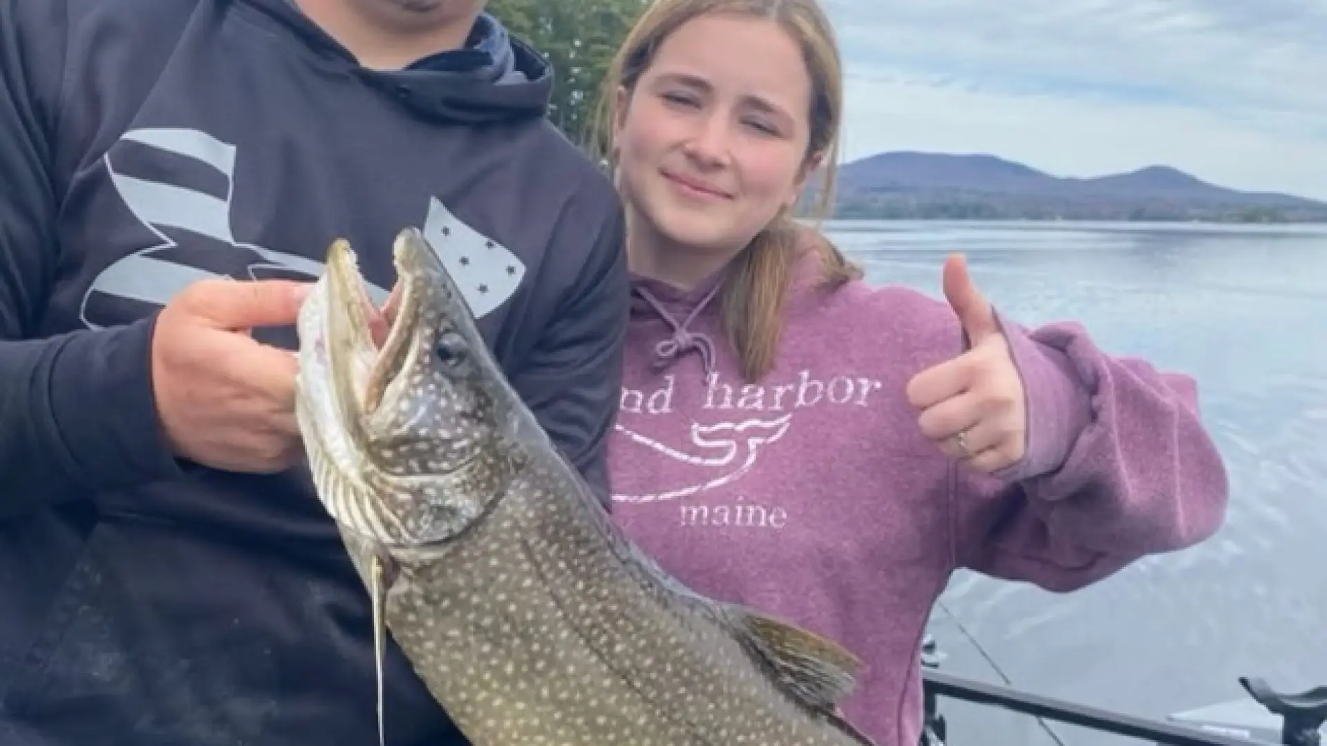 A man and woman hold a large fish and give a thumbs up.