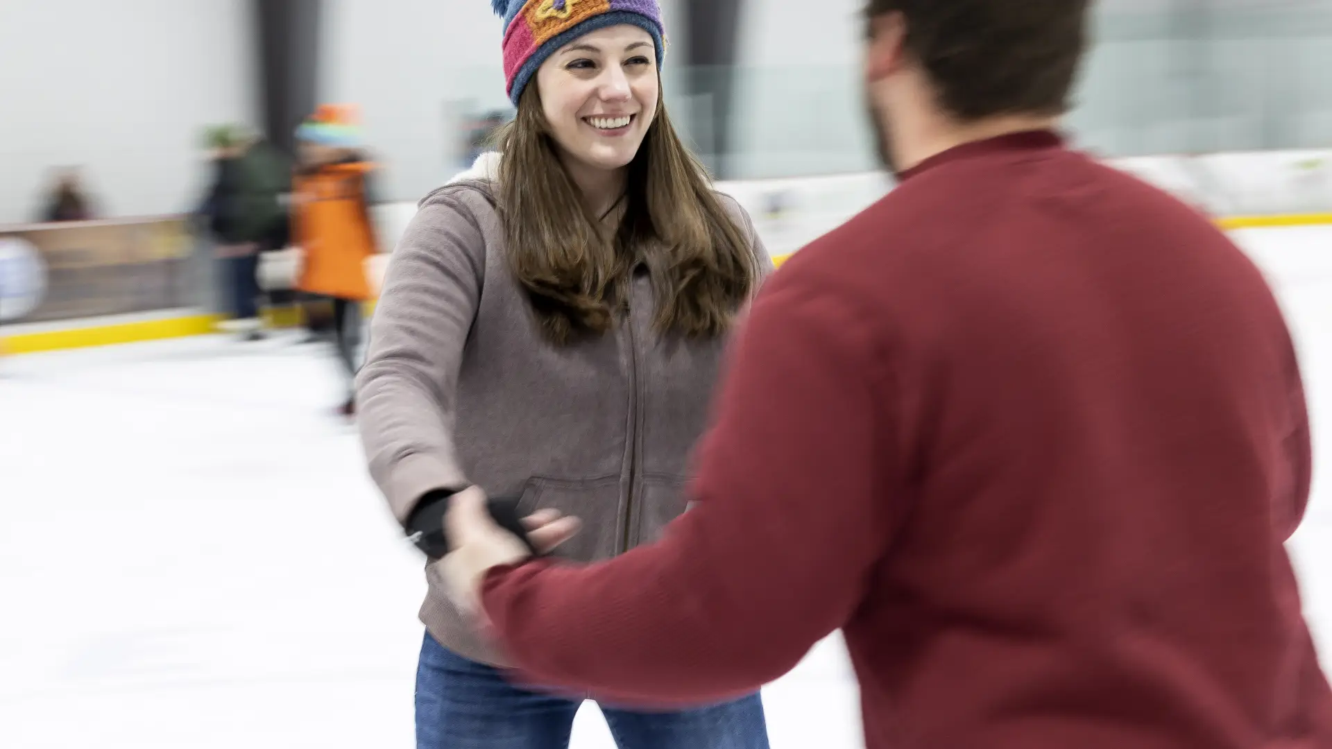 A smiling couple holding hands tentatively on the ice.