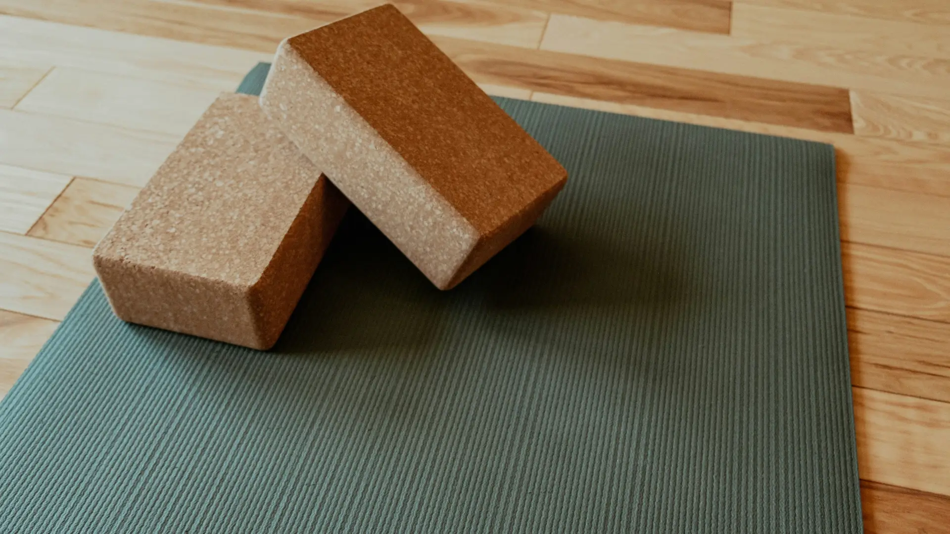 Two cork yoga blocks rest on a textured grey yoga mat spread across a light-colored hardwood floor.