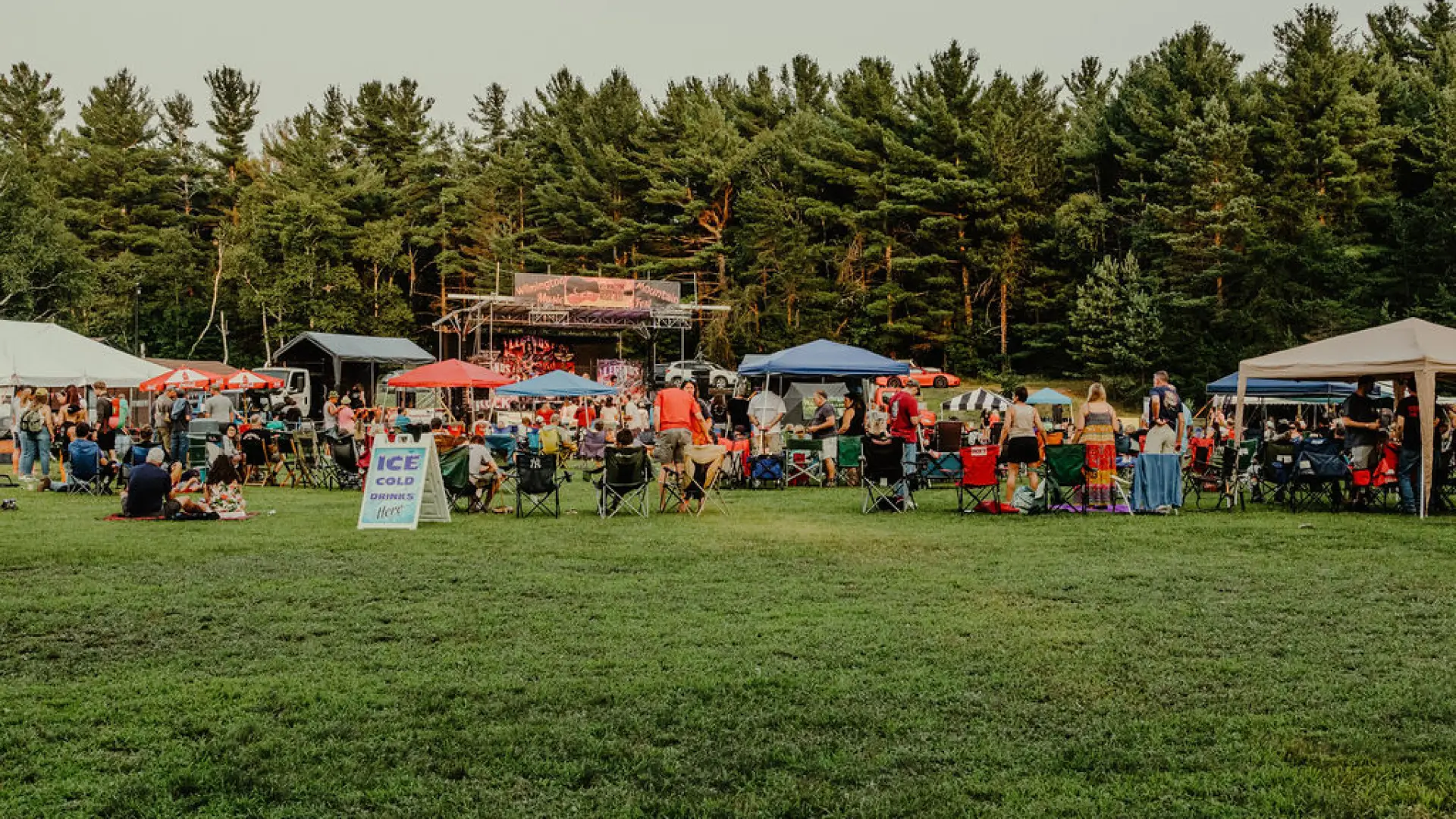 View of music festival crowd and stages from across a green field in summer