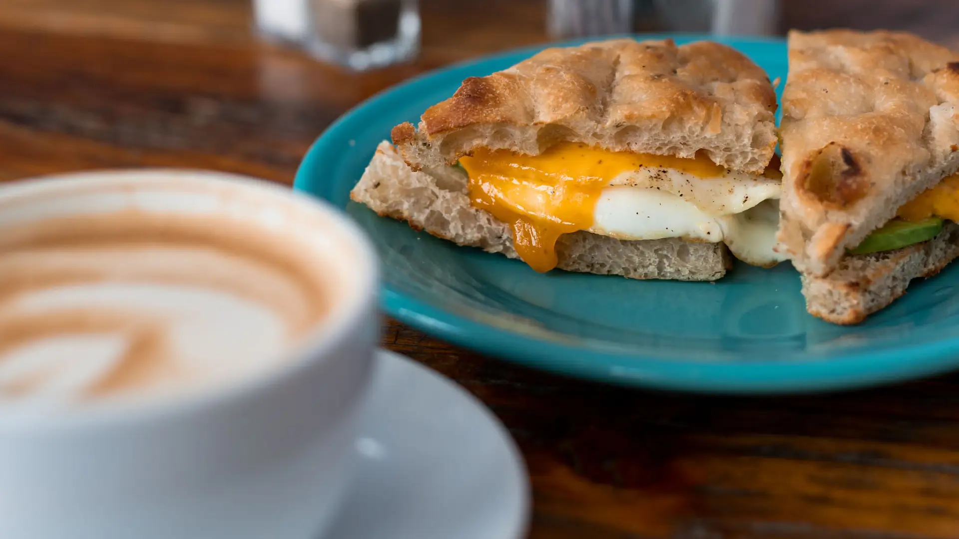 Egg sandwich on a fluffy english muffin next to a latte.