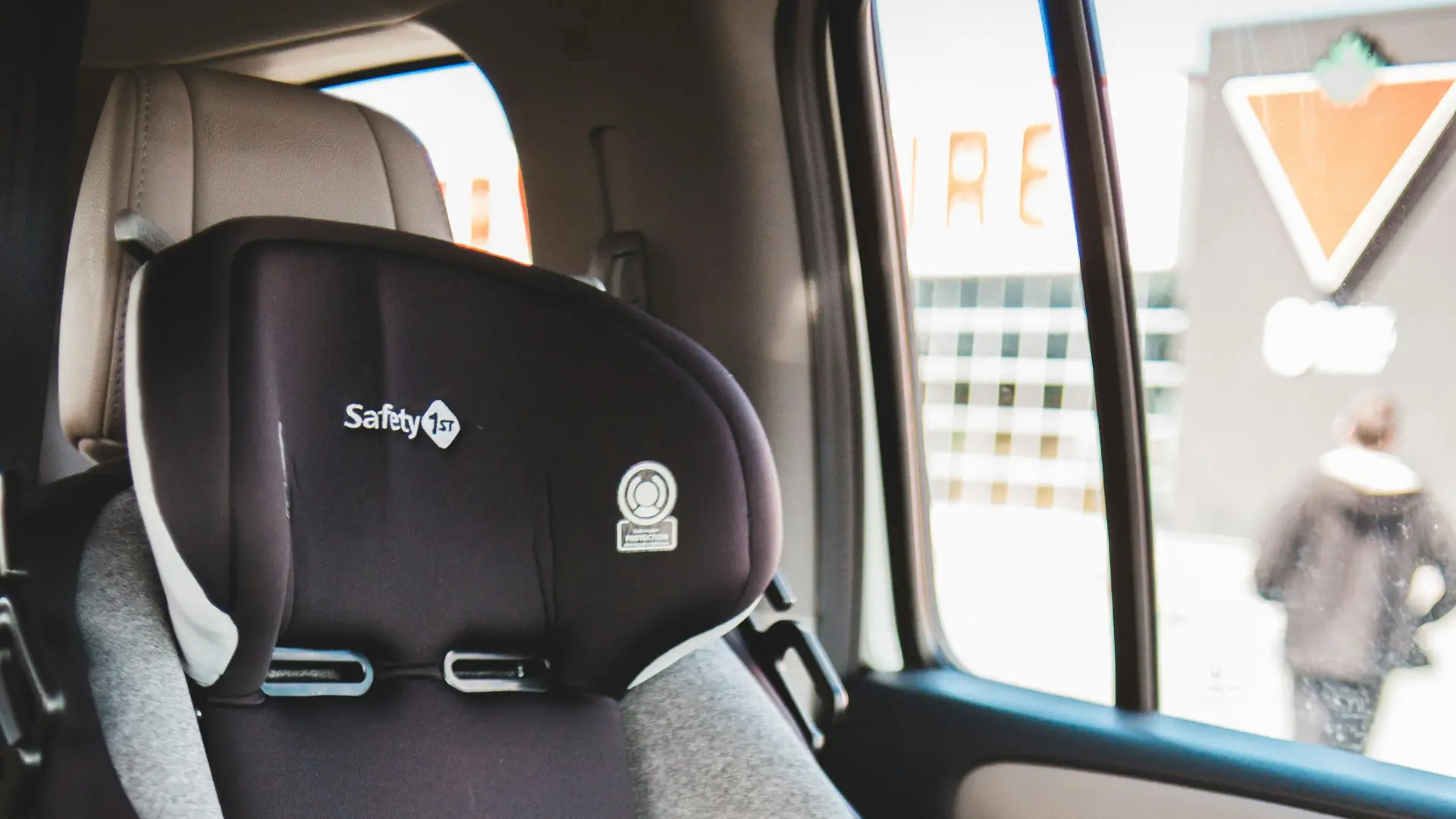 A black and gray Safety 1st car seat is installed in the backseat of a vehicle, with children's books resting next to it.