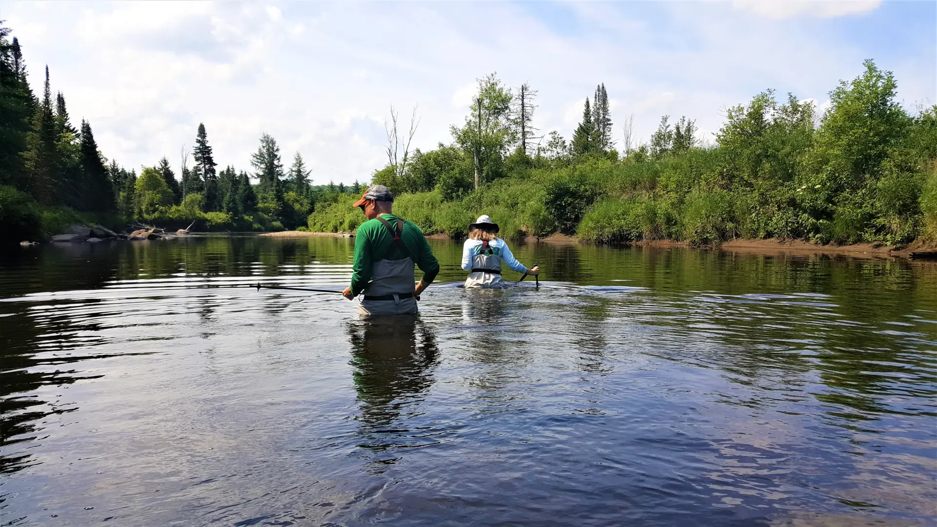 People in chest wadders walk through the slow flowing river