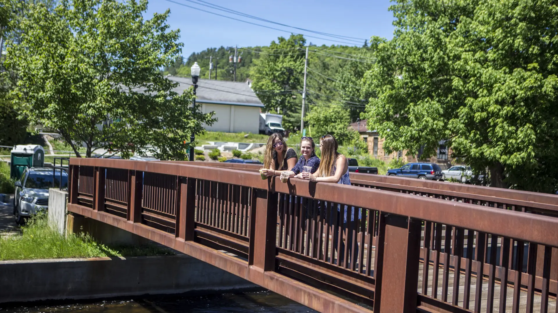 Three girls rest and soak up the view on the bridge along the Saranac Lake Riverwalk.