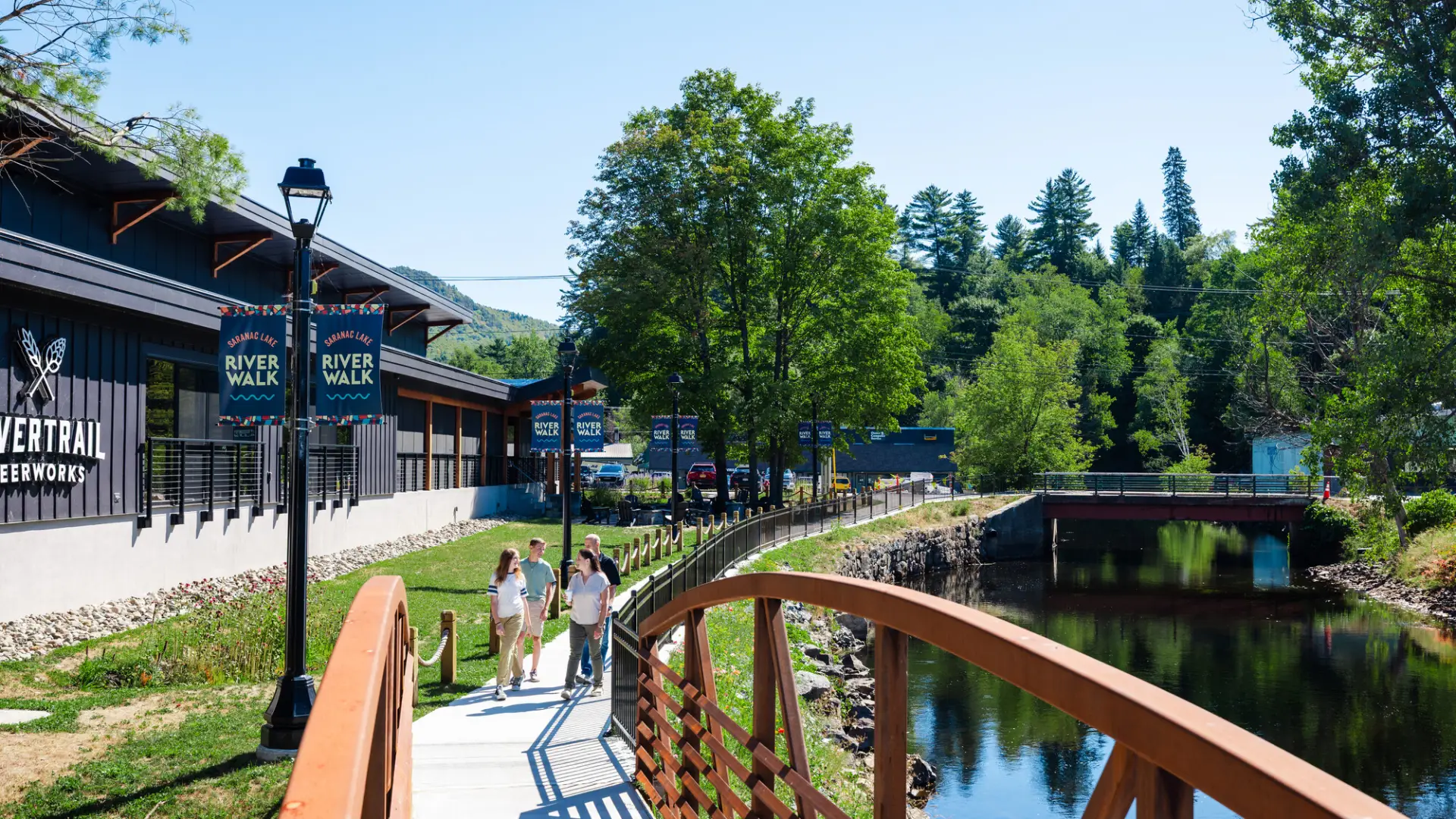 A family walks a trail along a river and brewery. 