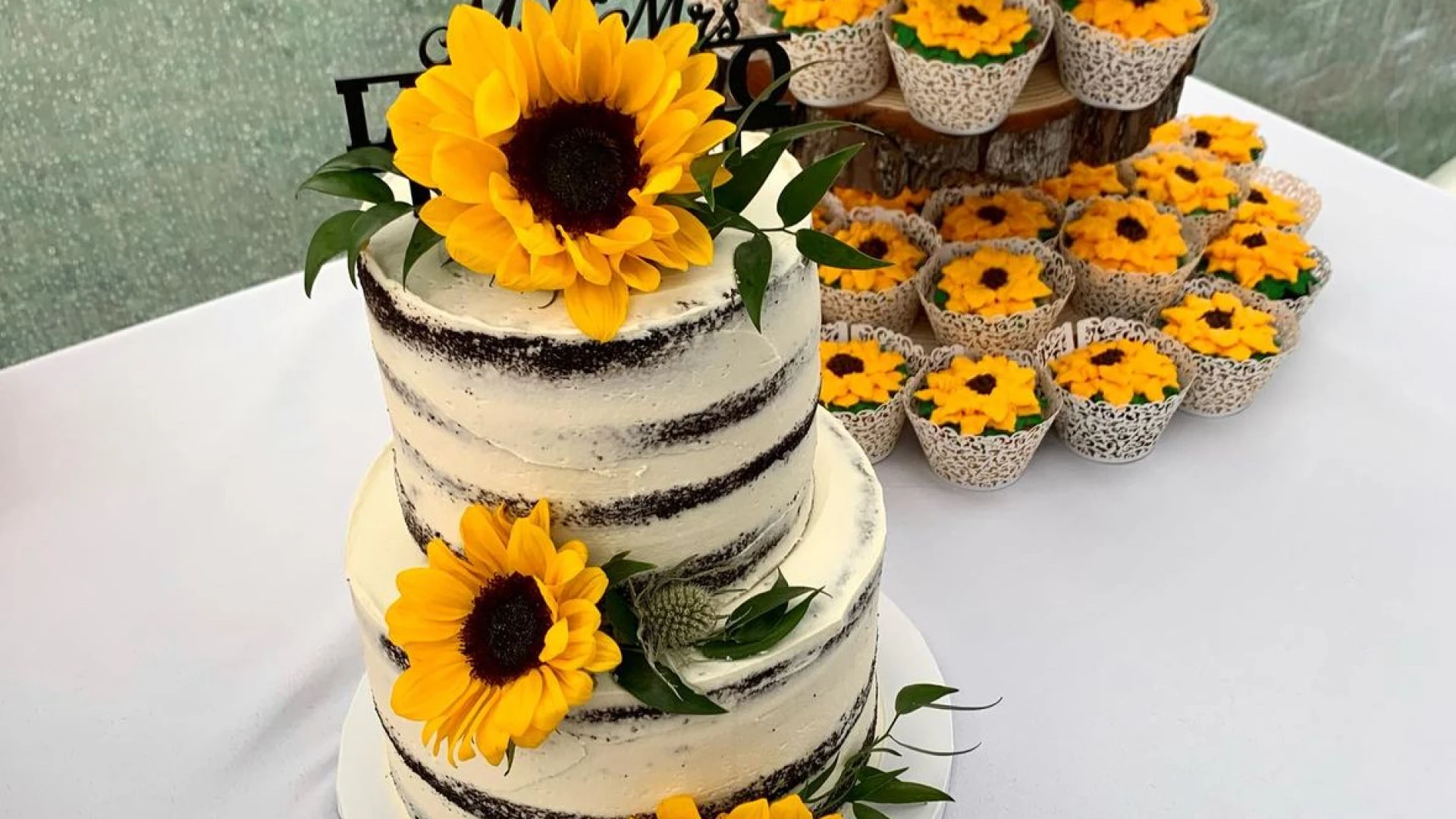 A multi tiered cake, frosted to look like paper birch, with sunflowers and sunflower cupcakes.