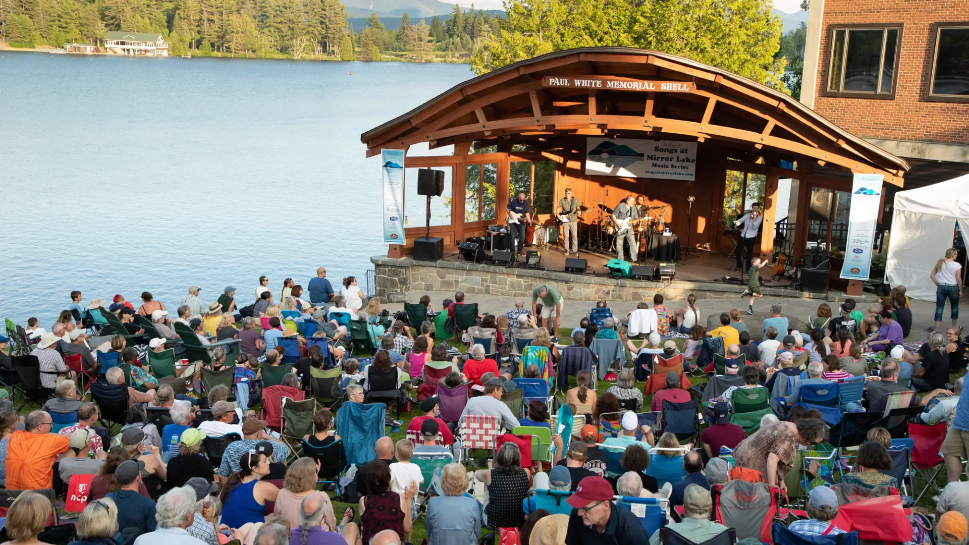 Crowd gathers in Mid's Park on a summer evening to listen to live music.