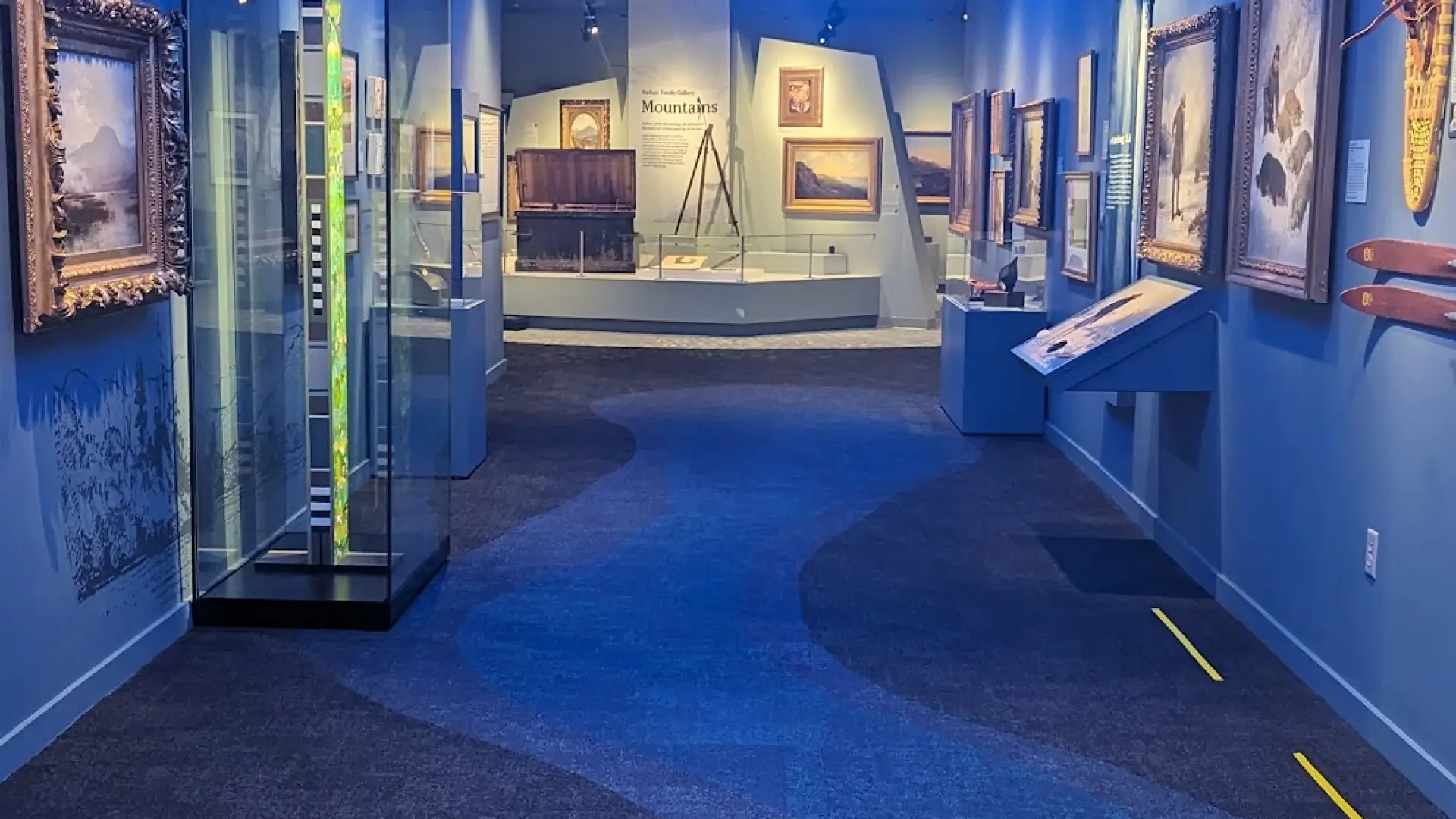 Art pieces on display in a long hallway with blue decor on walls, floor & ceiling which resembles waves.
