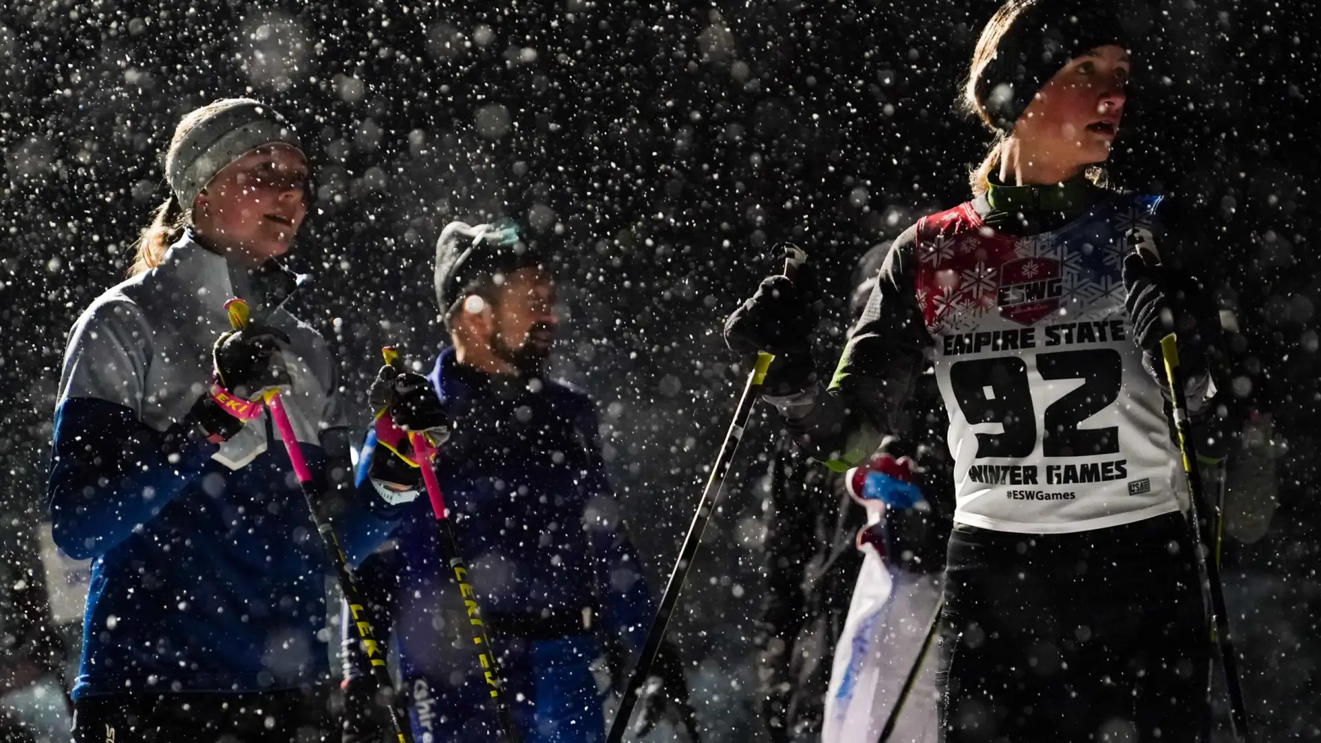 Athletes preparing for cross-country skiing in a snowy atmosphere at the Empire State Winter Games. Snowflakes fill the air.