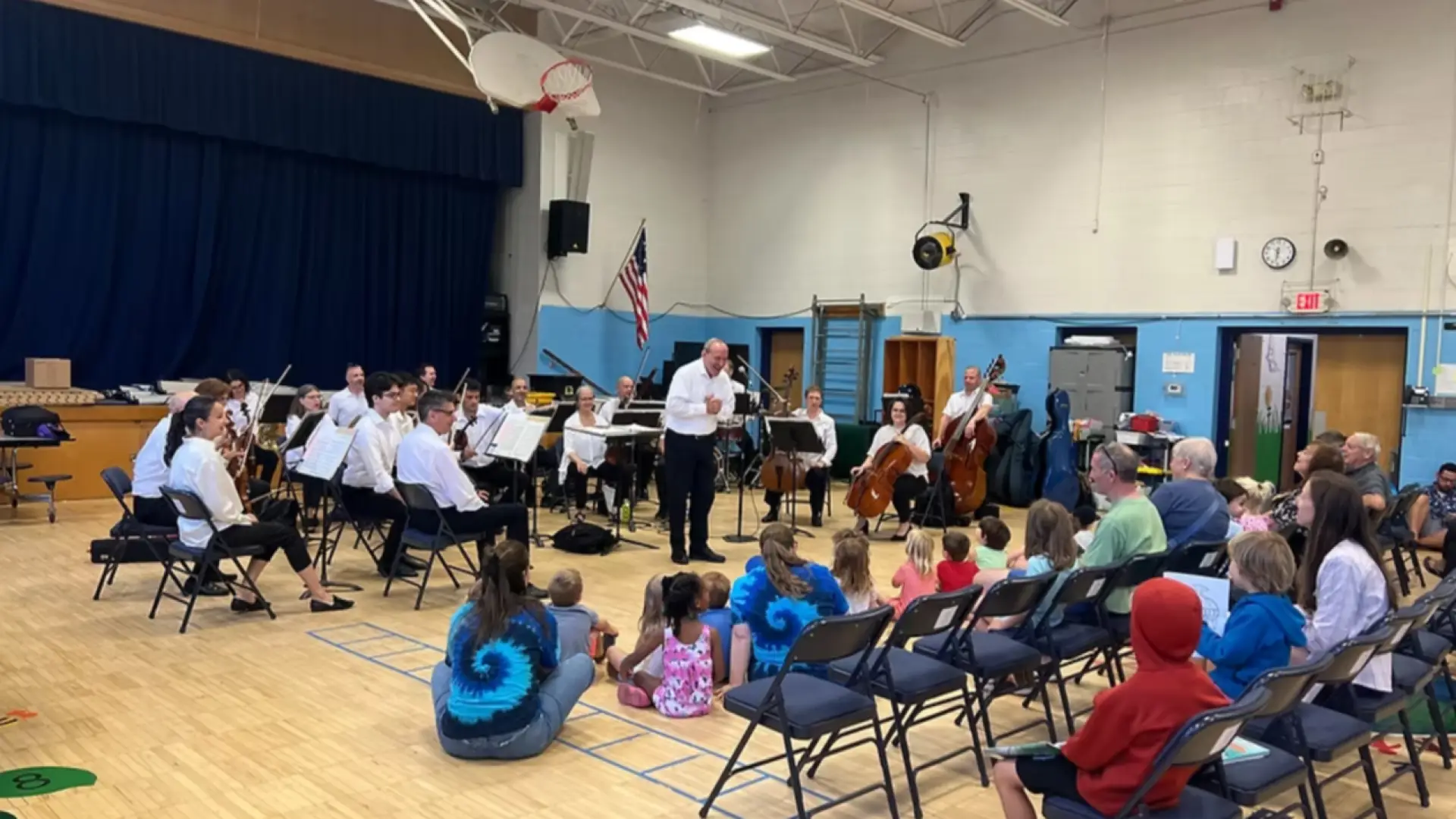 Lake Placid Sinfonietta set up in gym of school with children and parents sitting on floor and in rows of folding chairs