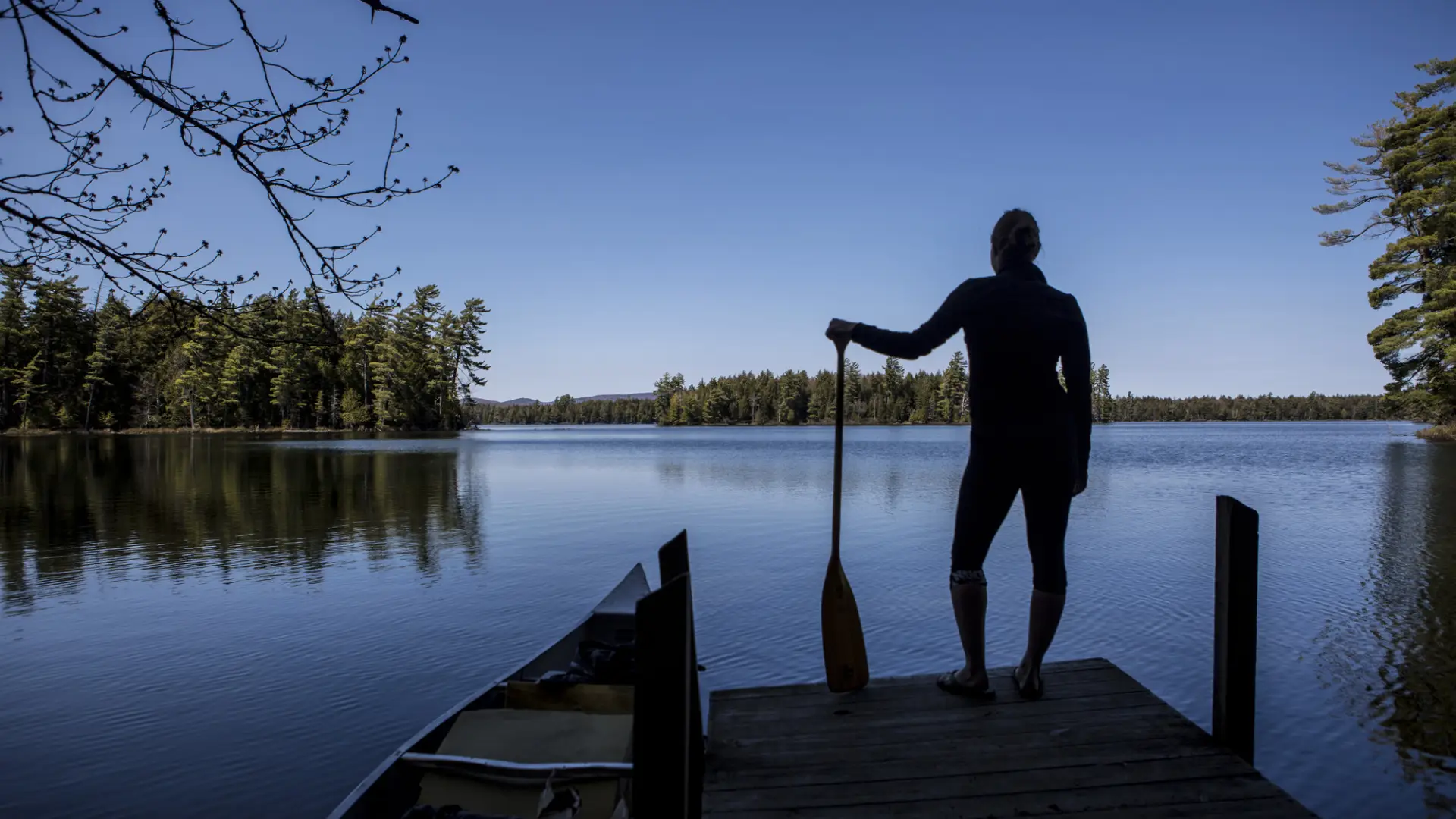 A paddler at the edge of a short, wooden dock by the water