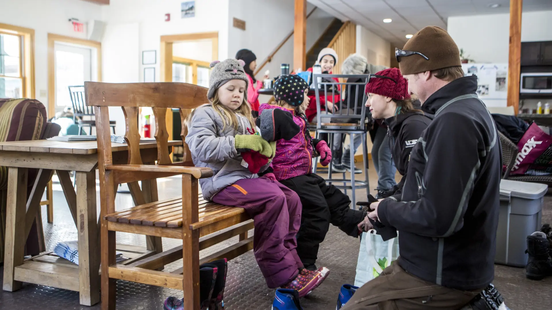 A father and mother help their kids put on ski boots as they sit on a bench inside the Dewey Mountain lodge.