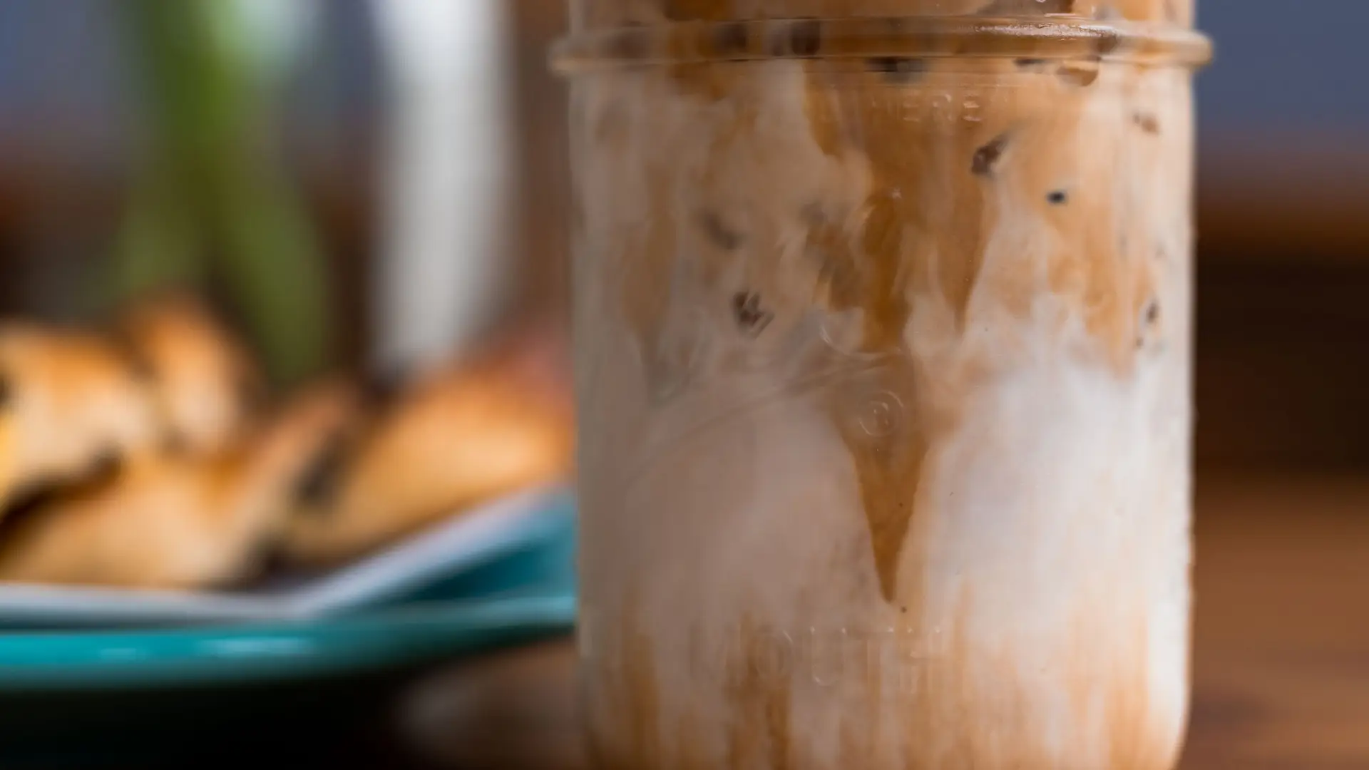An iced coffee in a mason jar next to breakfast on a plate.