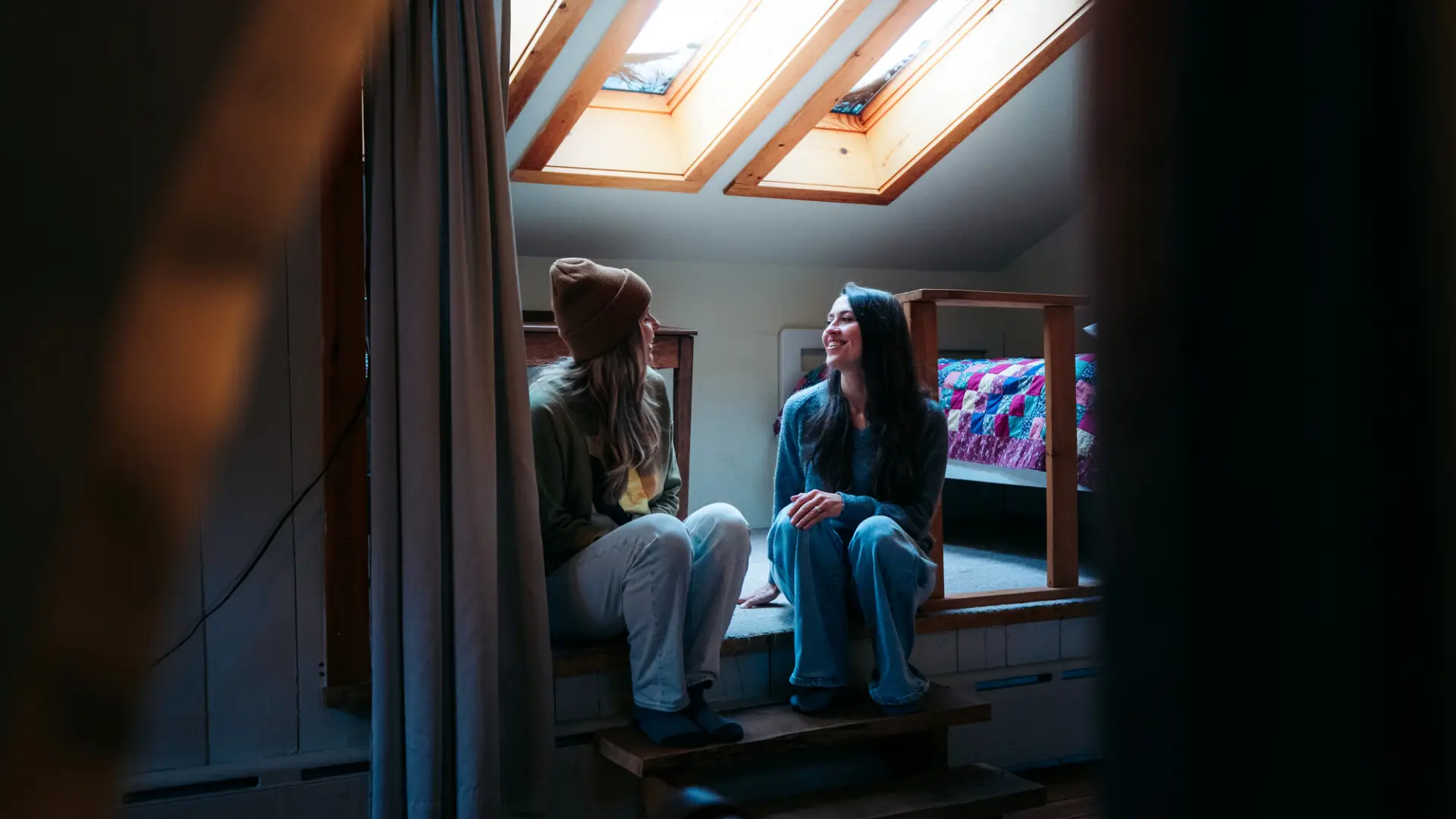 Two women talk in the cove of a cabin.
