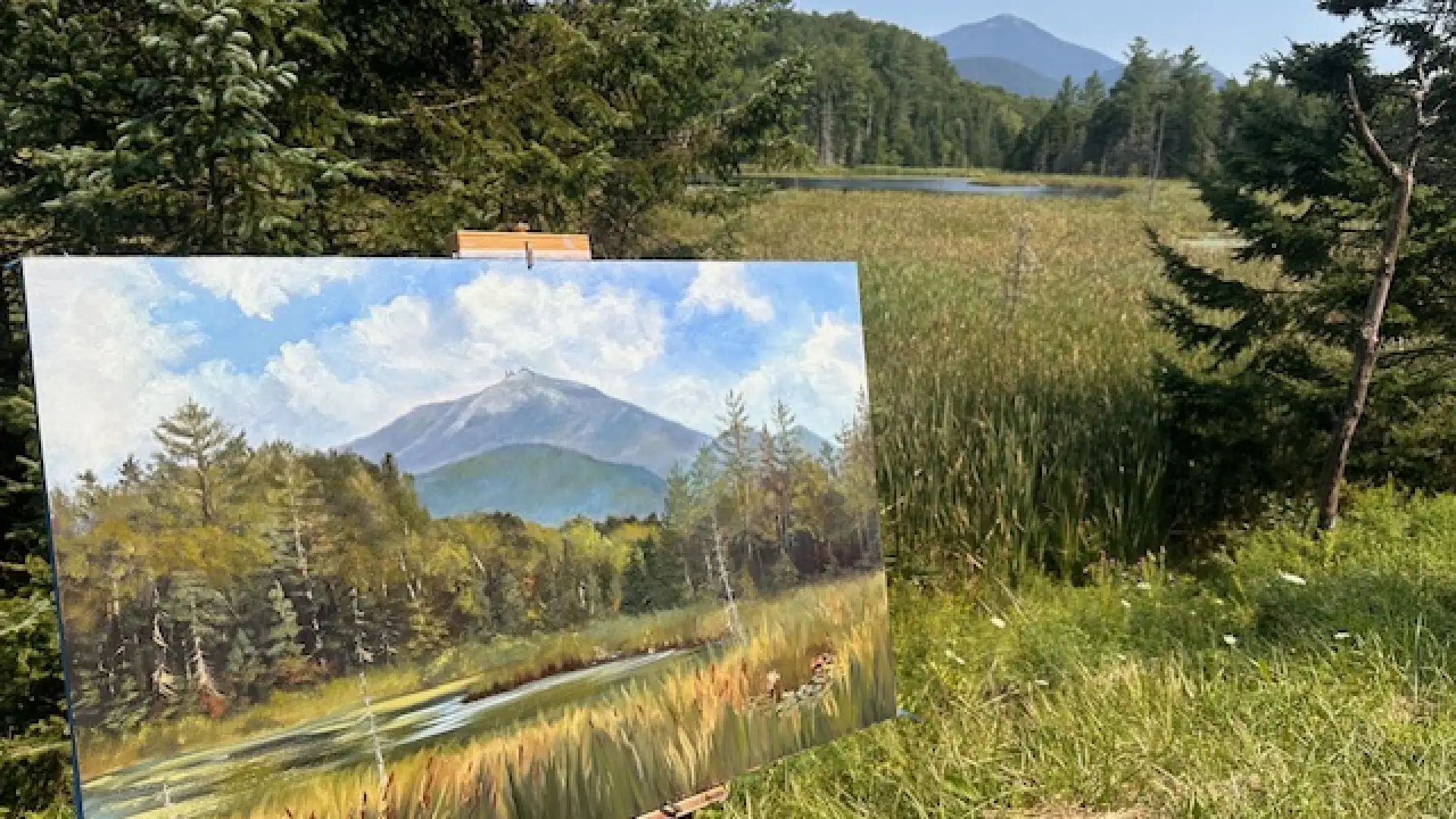 The artist's view of a plein air painting underway while still attached to an easel while still overlooking the field, pine trees, swamp surrounding a river and mountain view that inspired the art.