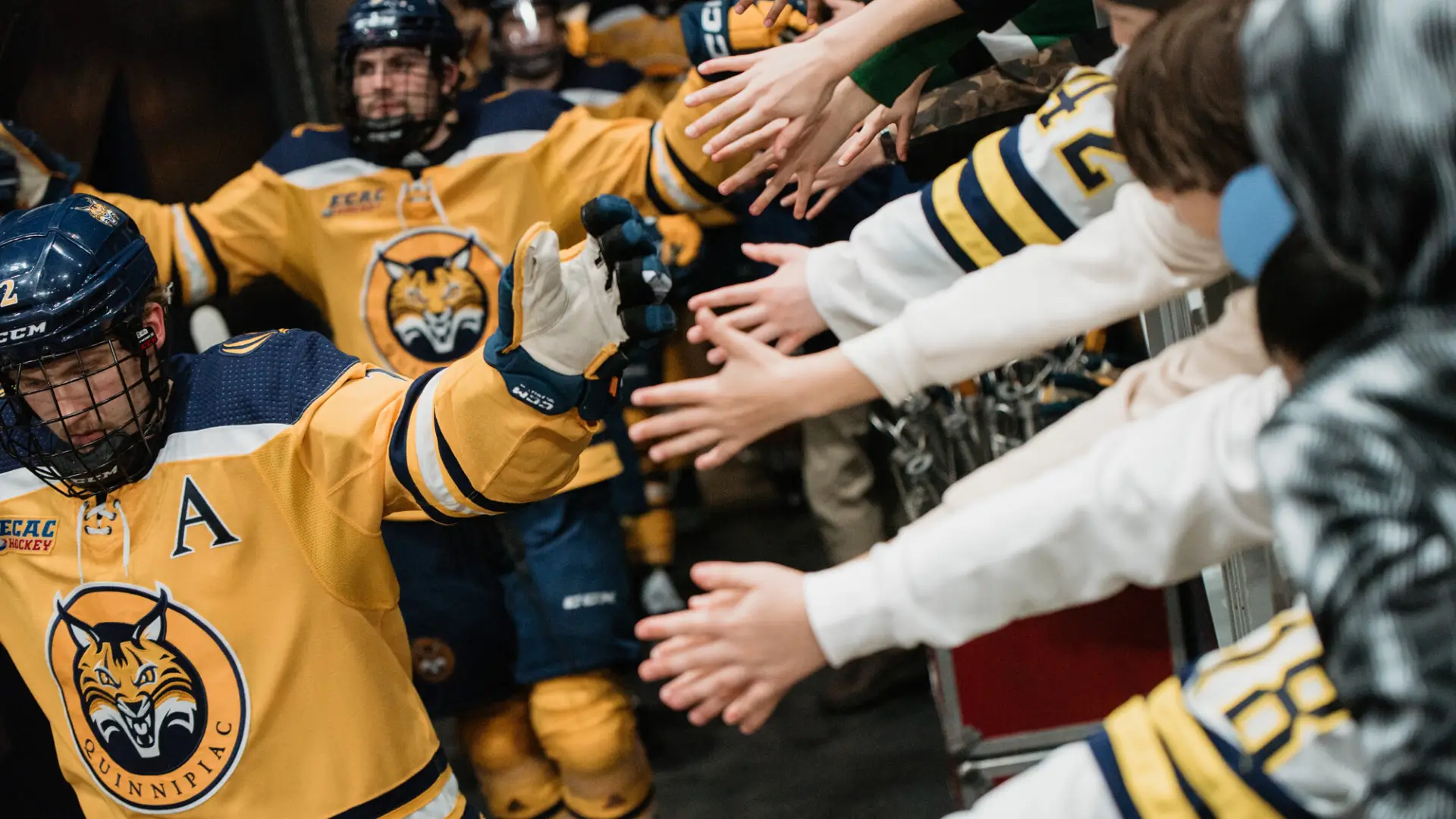 Quinnipiac hockey players high five hands hanging over partition as they leave the ice of the 1980 Herb Brooks Arena